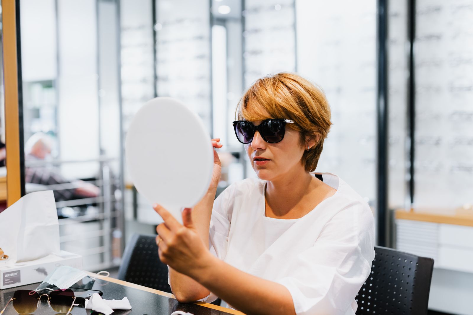 A customer checking new sunglasses in a hand mirror in an optician's shop