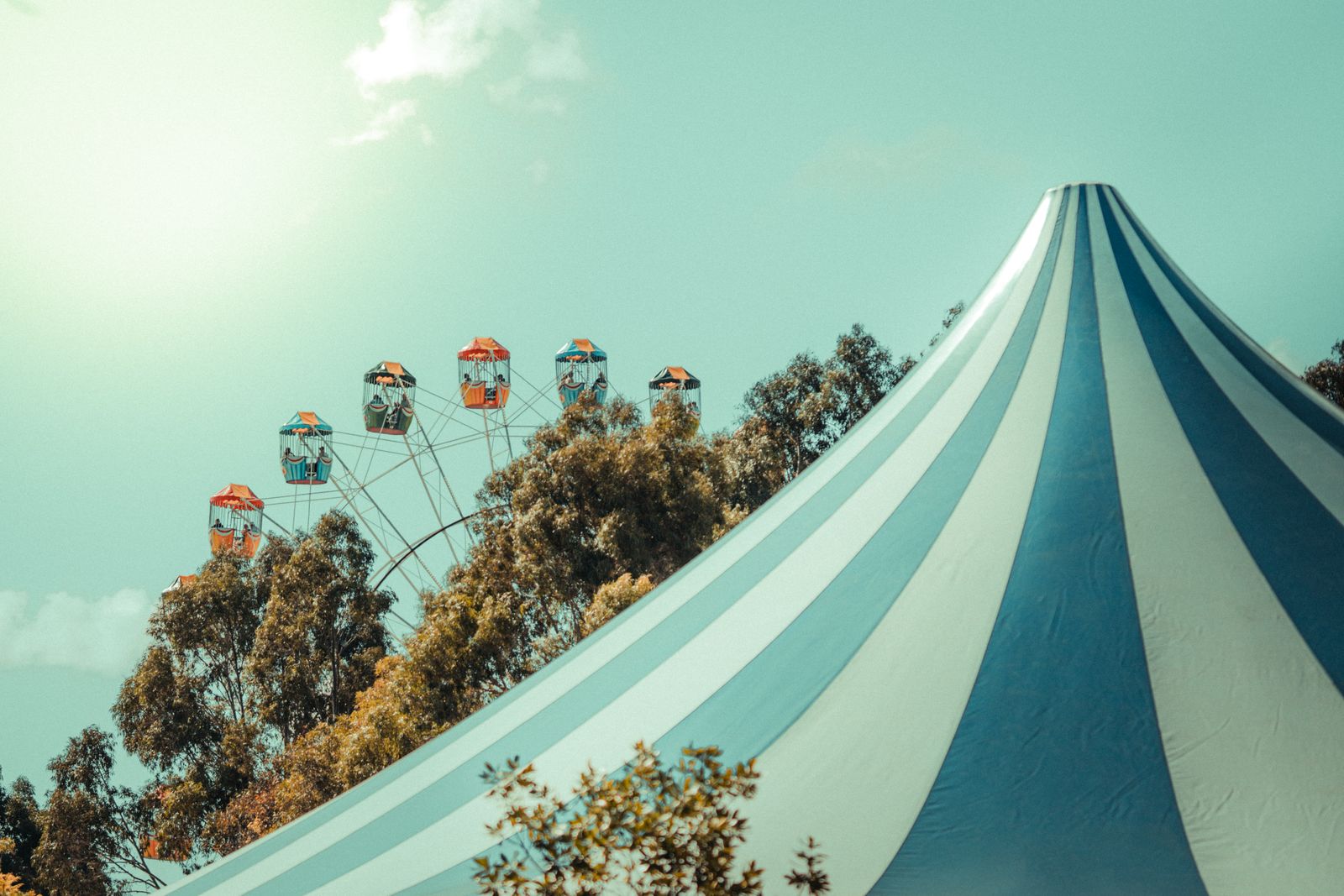 A striped circus-style tent beside a ferris wheel on a sunny day