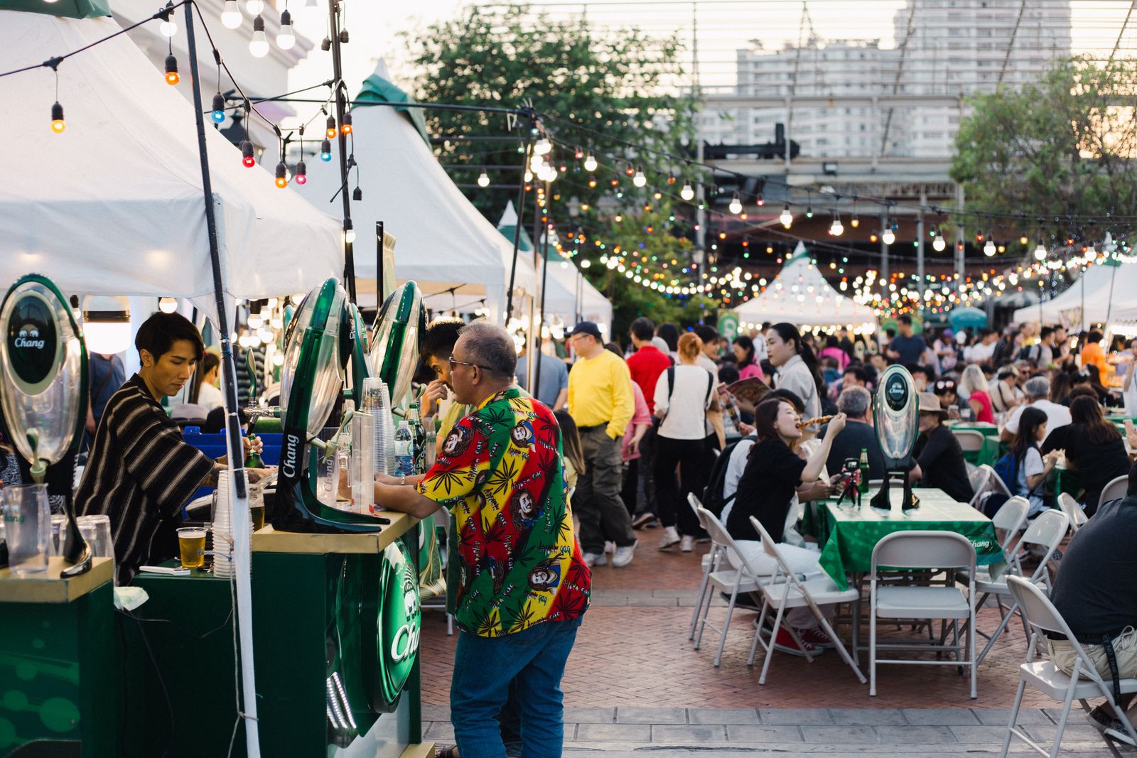Visitors at tables between food stalls and white tents at an outdoor festival