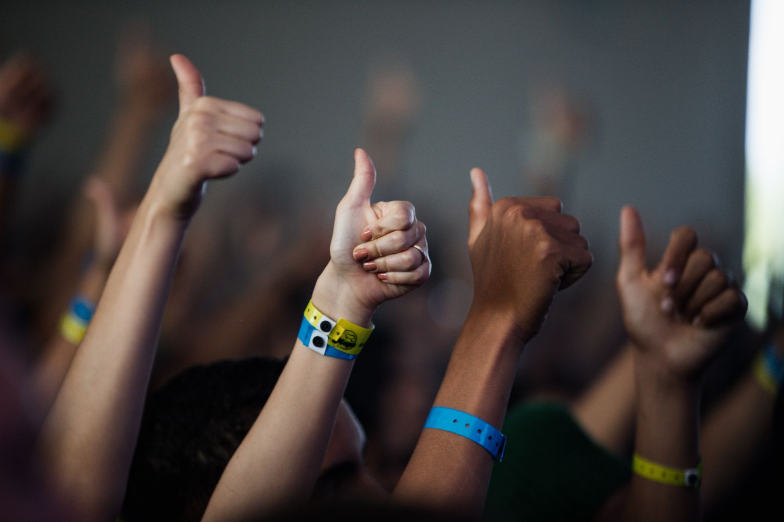 Raised hands giving a thumbs up, with festival wristbands on the wrists