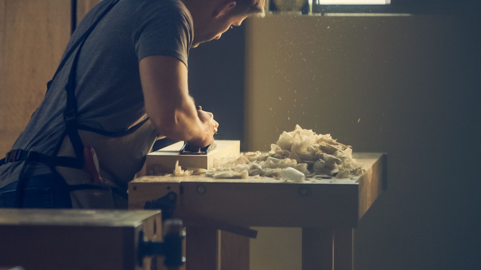 A joiner planing a board at a workbench covered in shavings