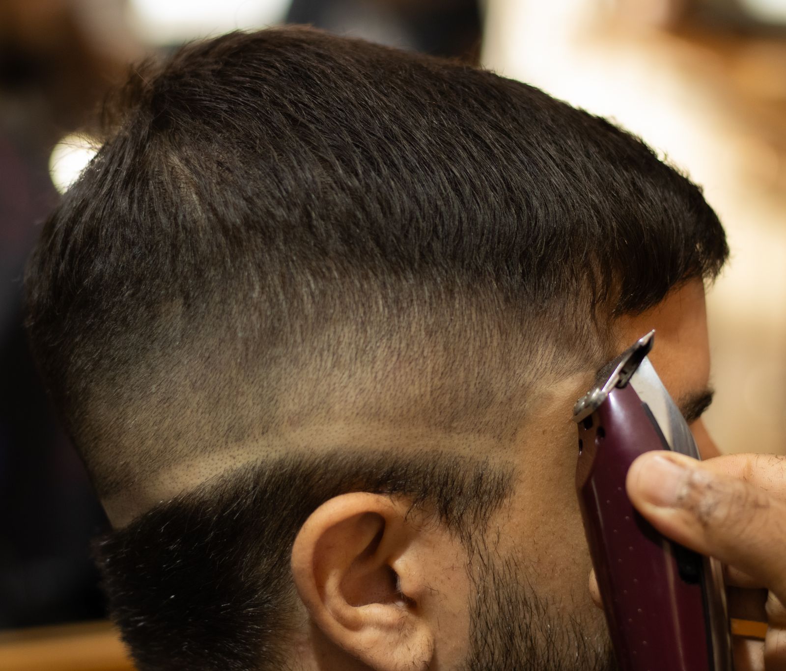 A barber working a fade up the side of a client's head with clippers