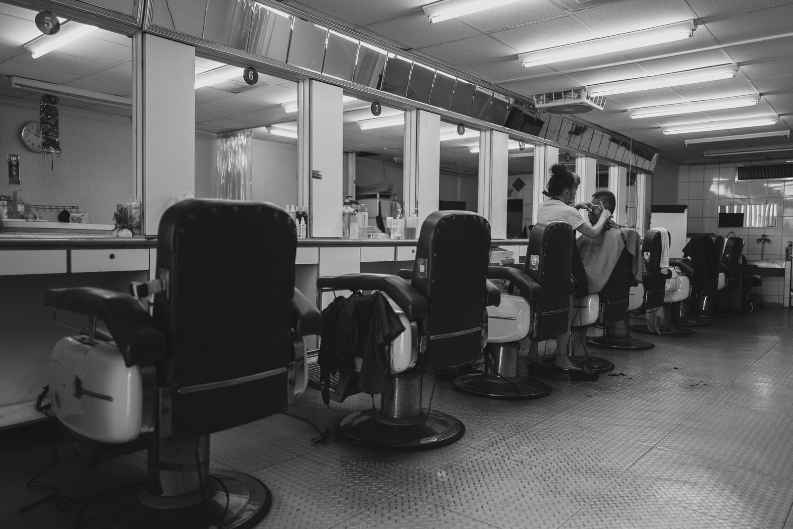 A long row of barber chairs and mirrors, in black and white