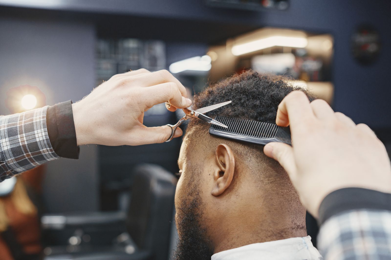 A barber cutting a client's hair with scissors over a comb