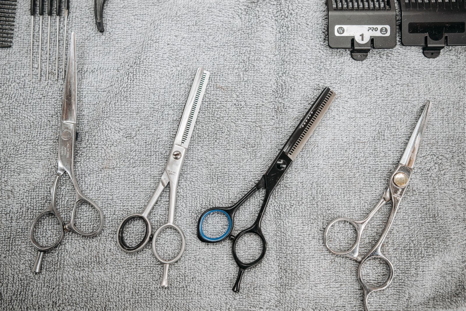 Scissors and thinning shears laid out on a grey towel beside a No. 1 clipper guard