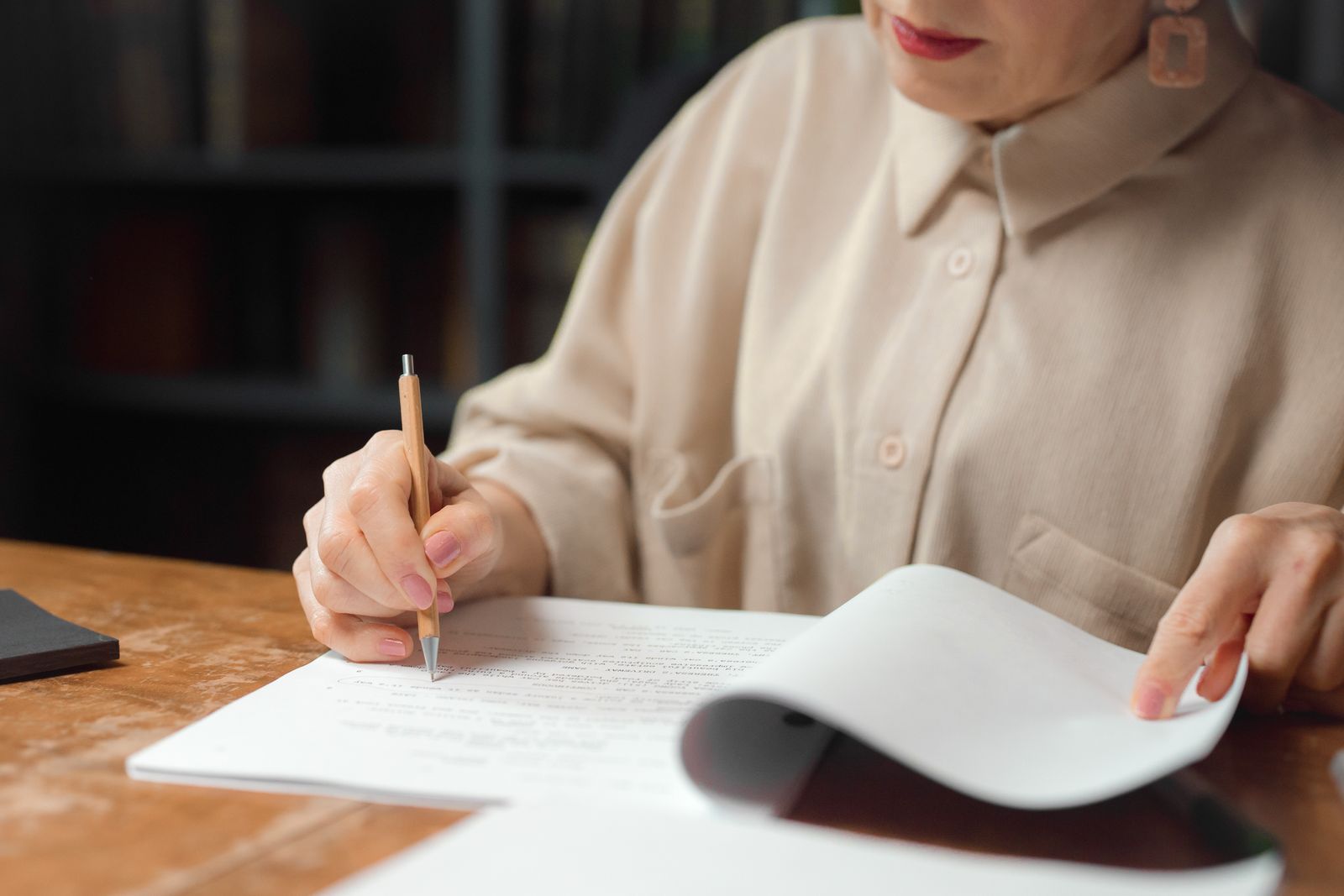 A person marking up printed pages with a pencil at a wooden desk