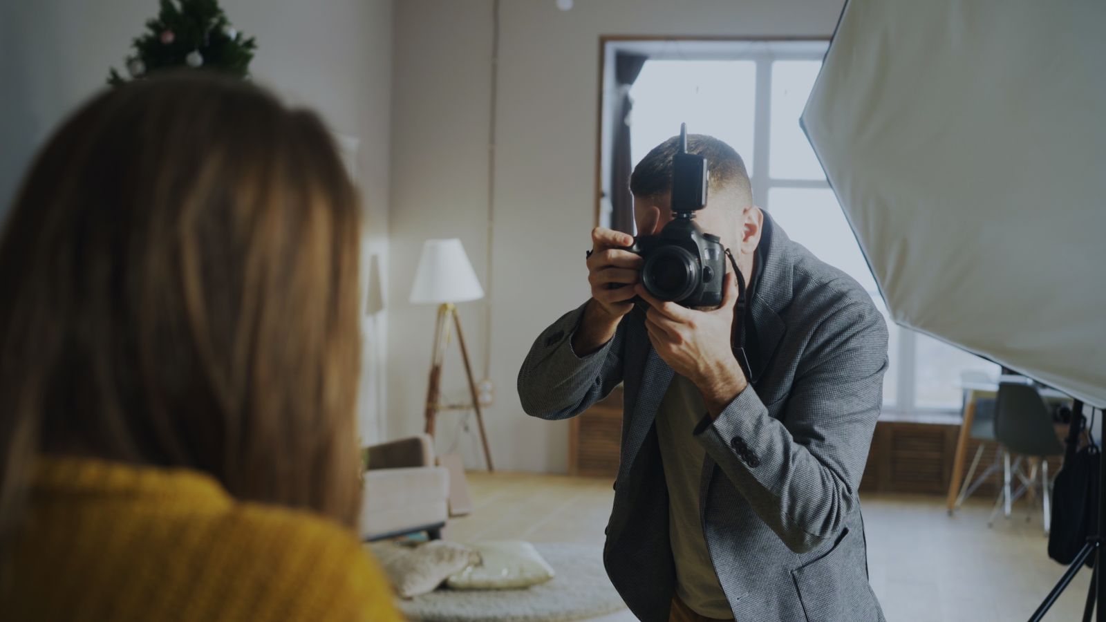 A portrait session seen over the client's shoulder, the photographer kneeling with his camera beside a softbox