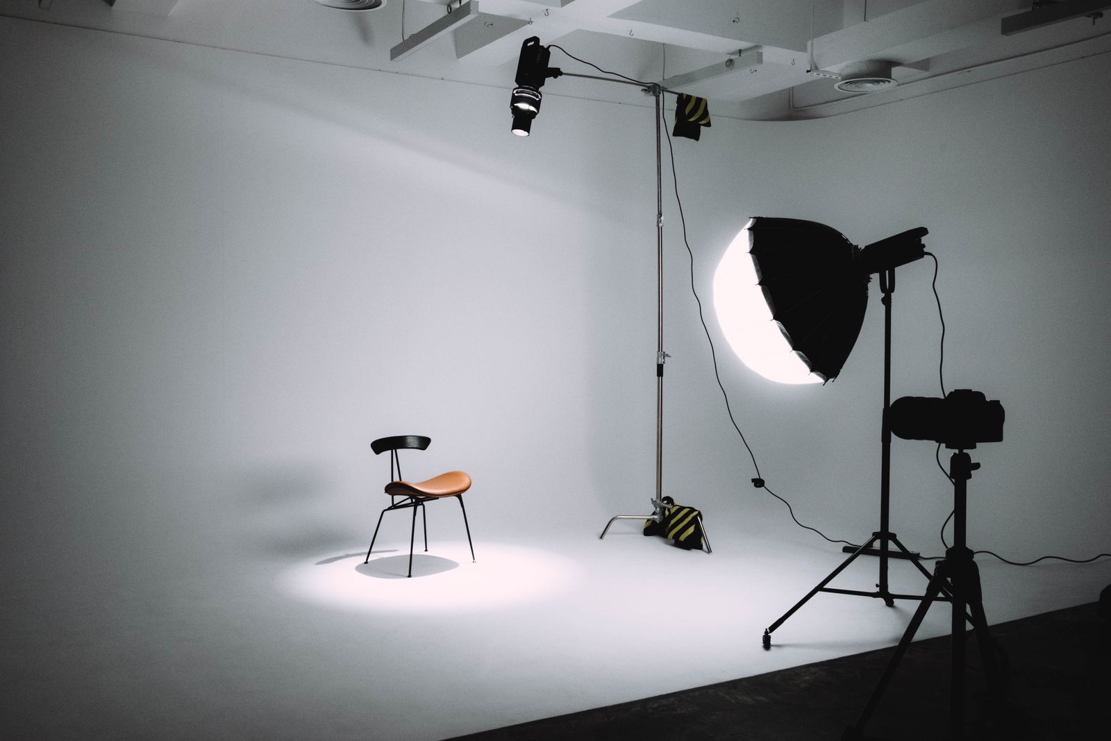 Photo studio with a white wall, one octabox light, a camera on a tripod and an empty chair