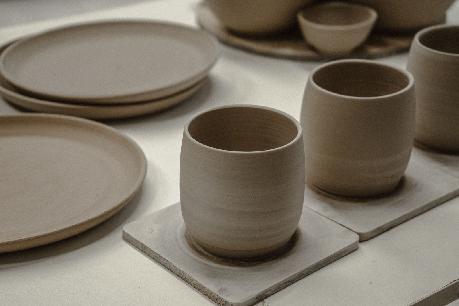 Handmade ceramic cups and plates in grey clay on a white table
