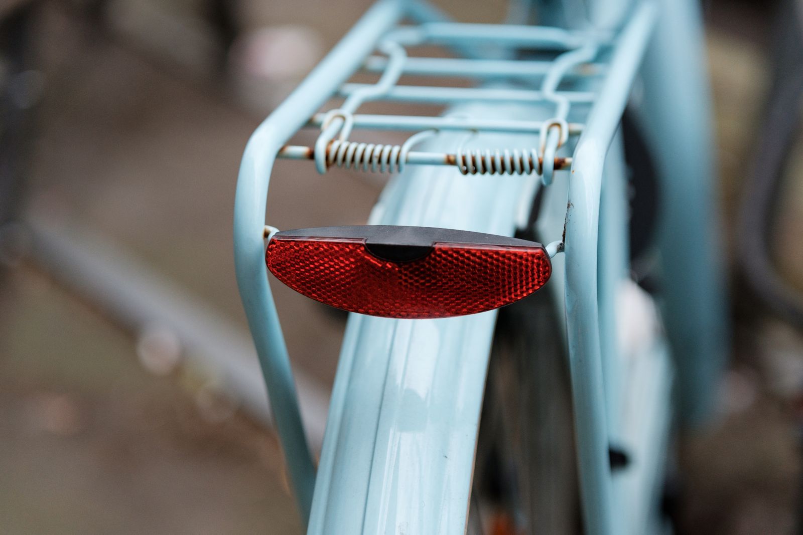 Close-up of a red rear light on the rack of a blue bicycle
