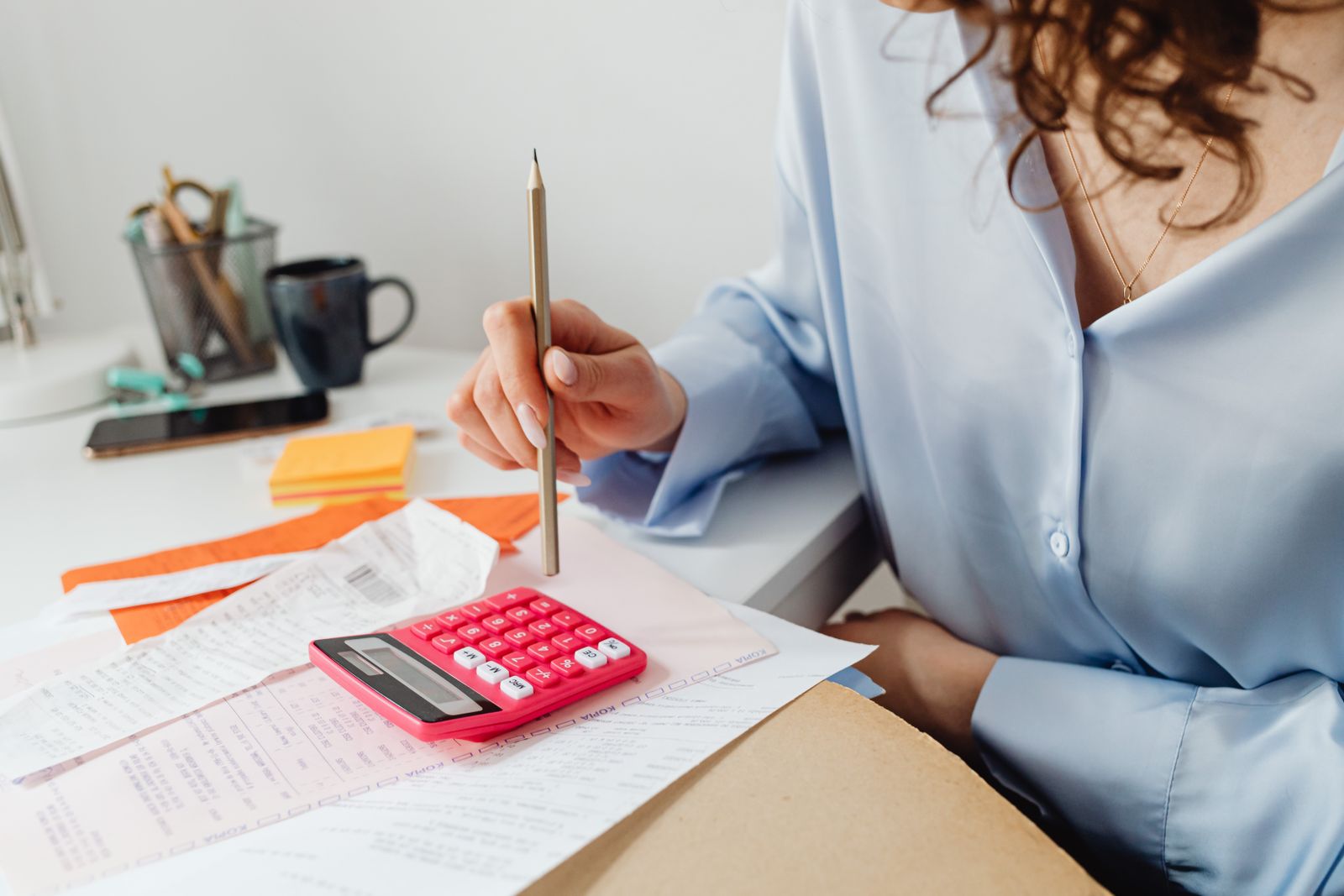 A woman working through figures with a calculator and papers at her desk