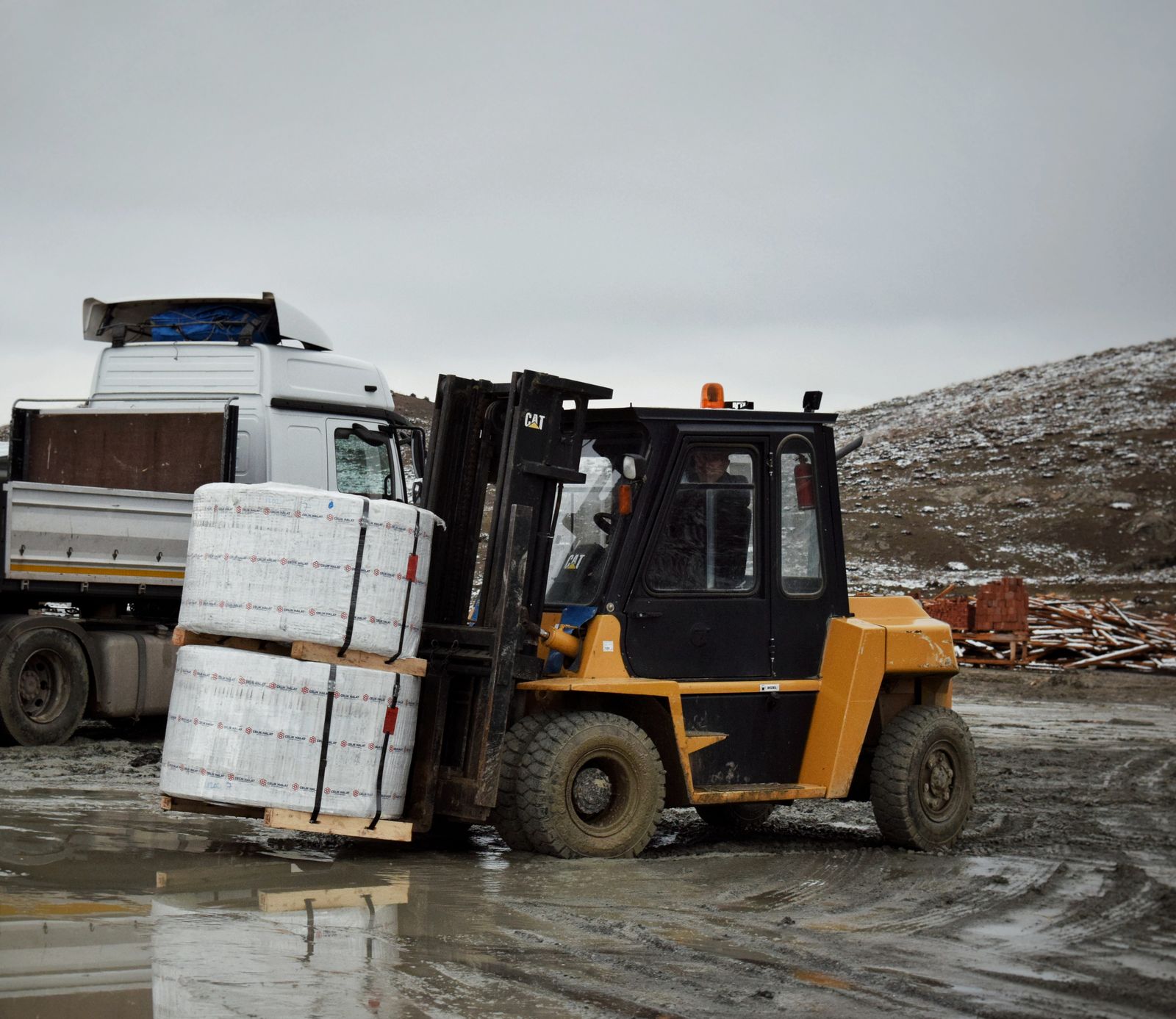 A forklift lifting wrapped pallets onto a flatbed truck in a yard