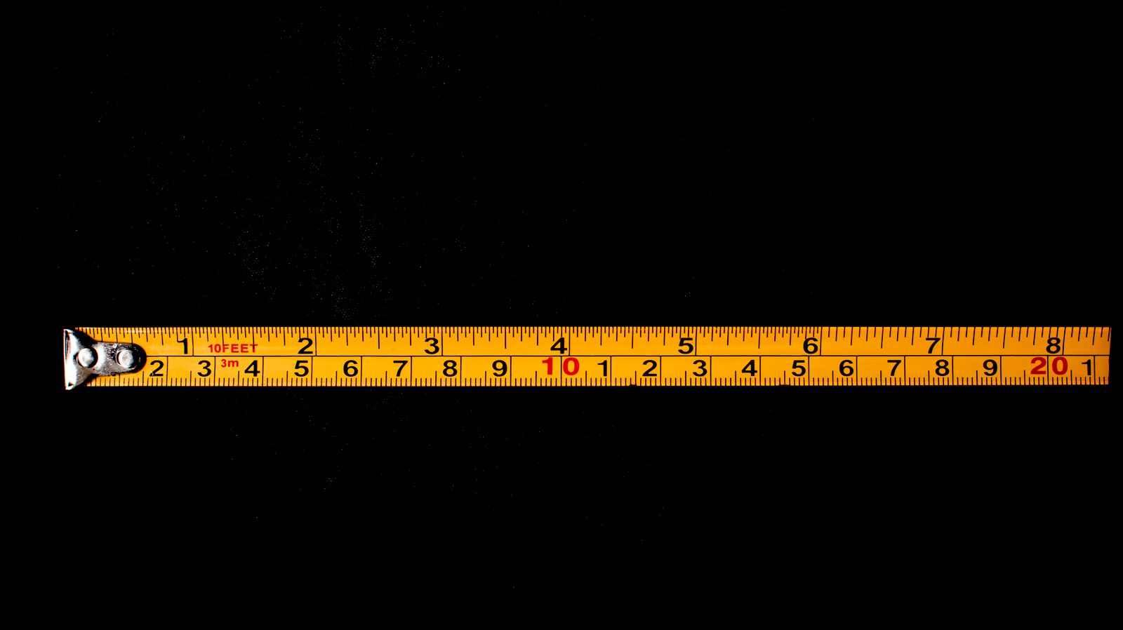 A yellow tape measure stretched out on a black surface