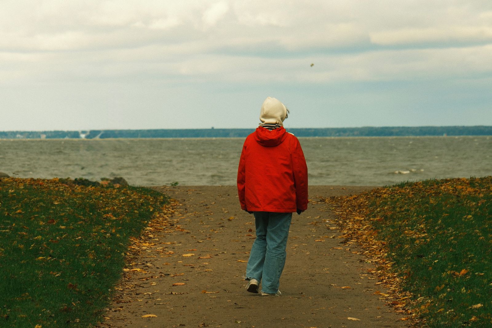 A person in a red jacket walking towards the sea on an autumn day