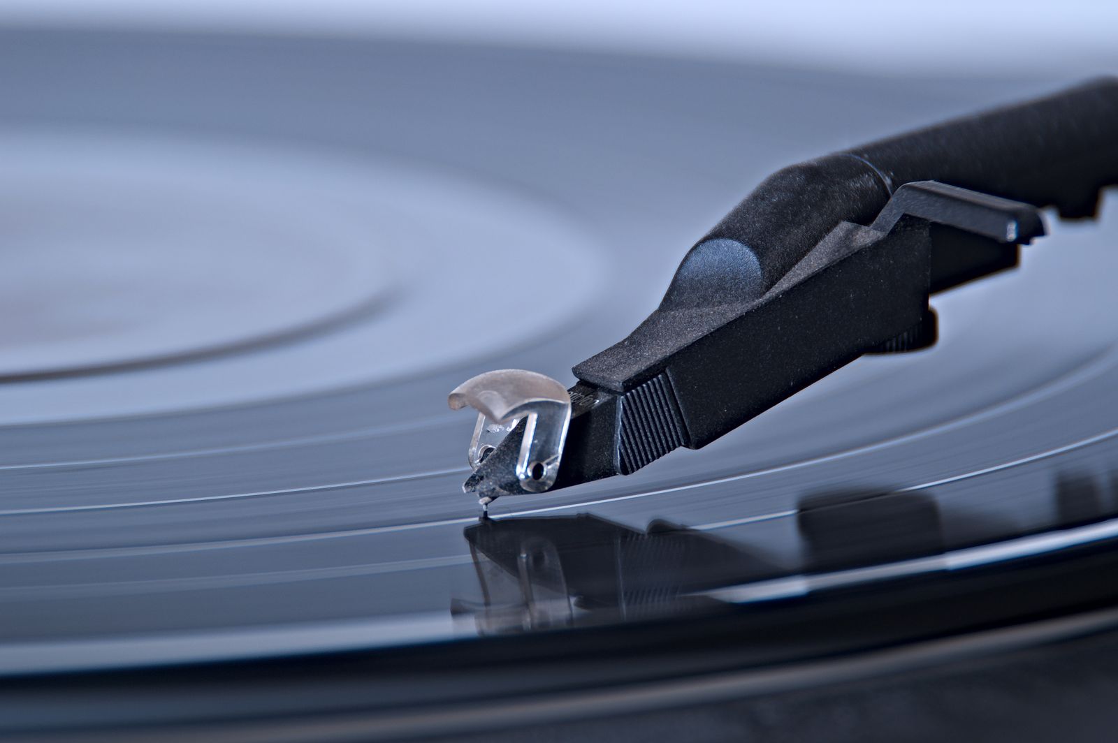 A stylus resting in the groove of a black record, in cool blue light