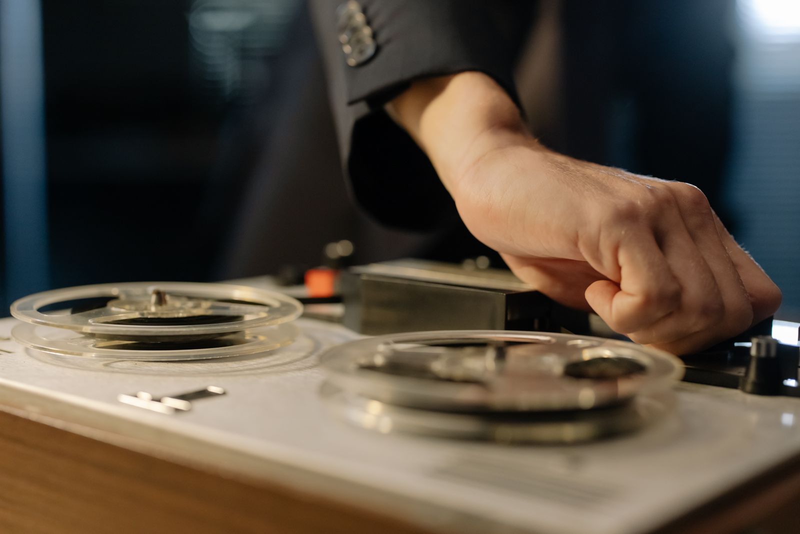 A hand pressing a key on an open-reel tape machine with two clear reels
