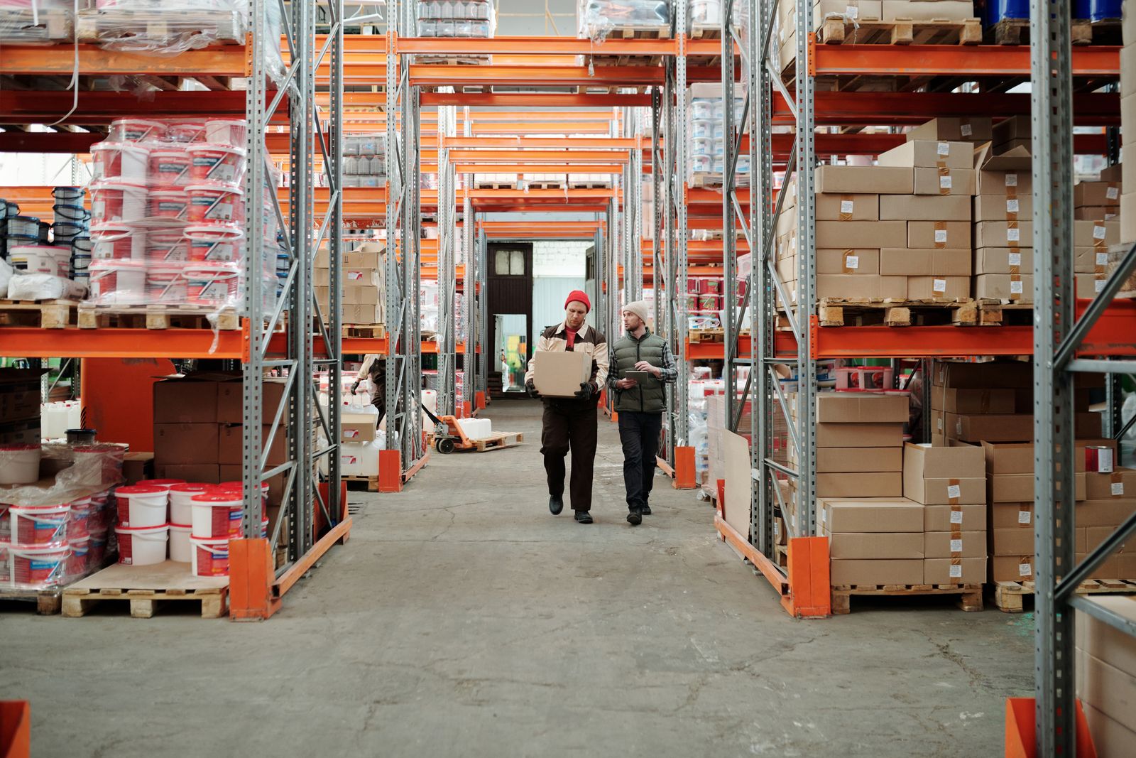 Two workers carrying a parcel along a warehouse aisle