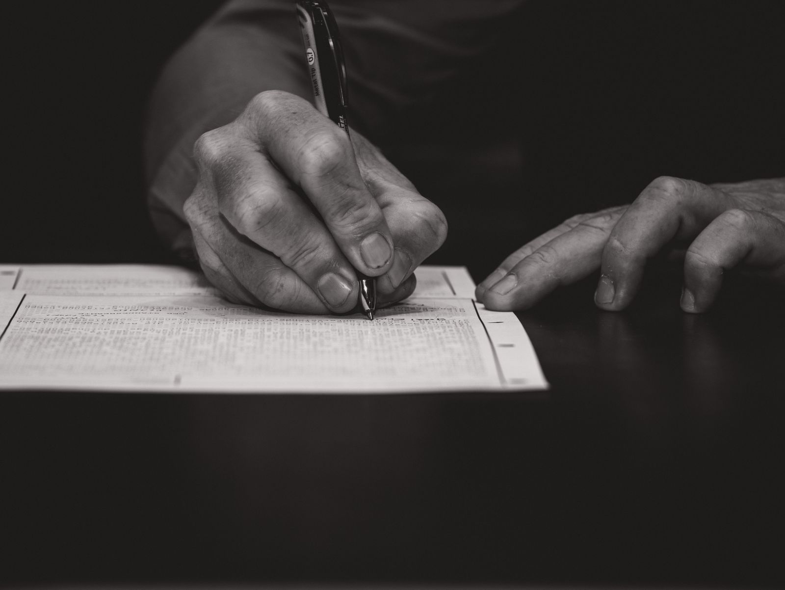 A hand signing a printed form with a pen, in black and white