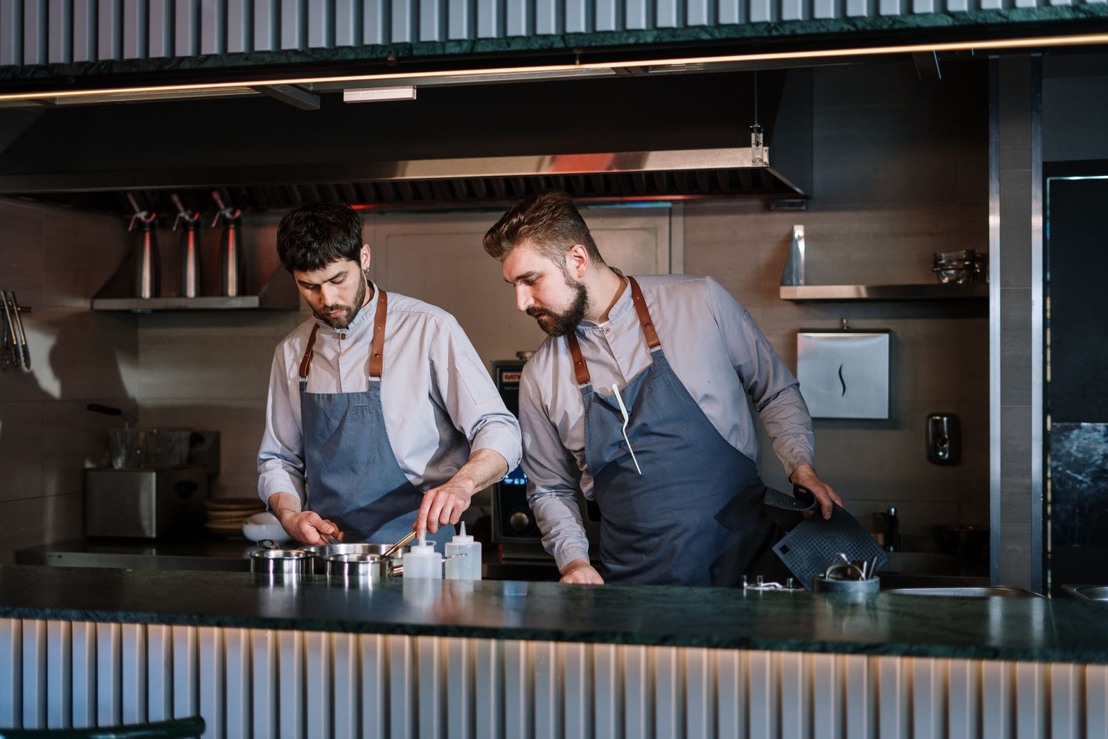 Two cooks in aprons working side by side in an open restaurant kitchen