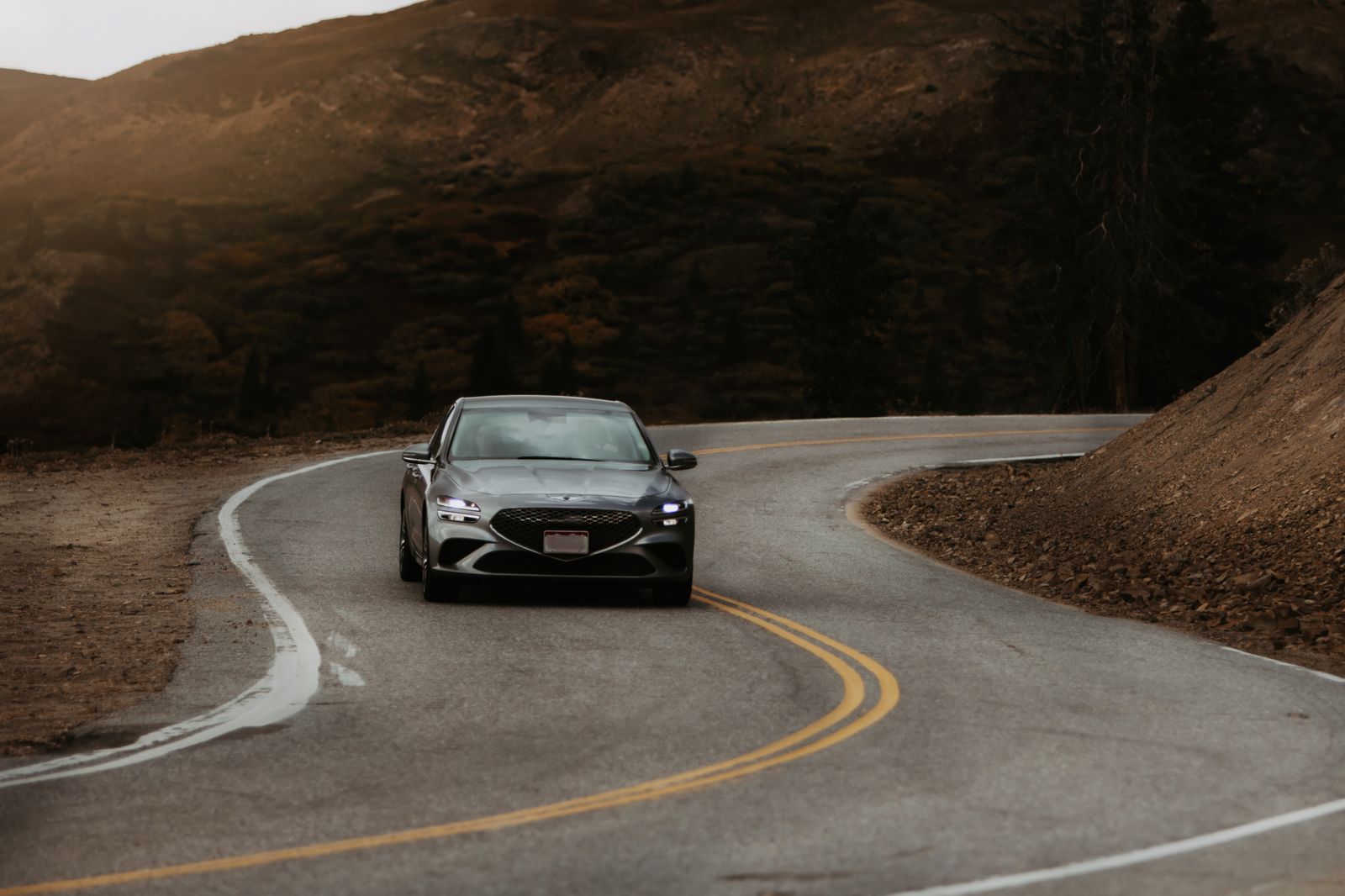 A grey saloon coming round a bend on a mountain road at dusk