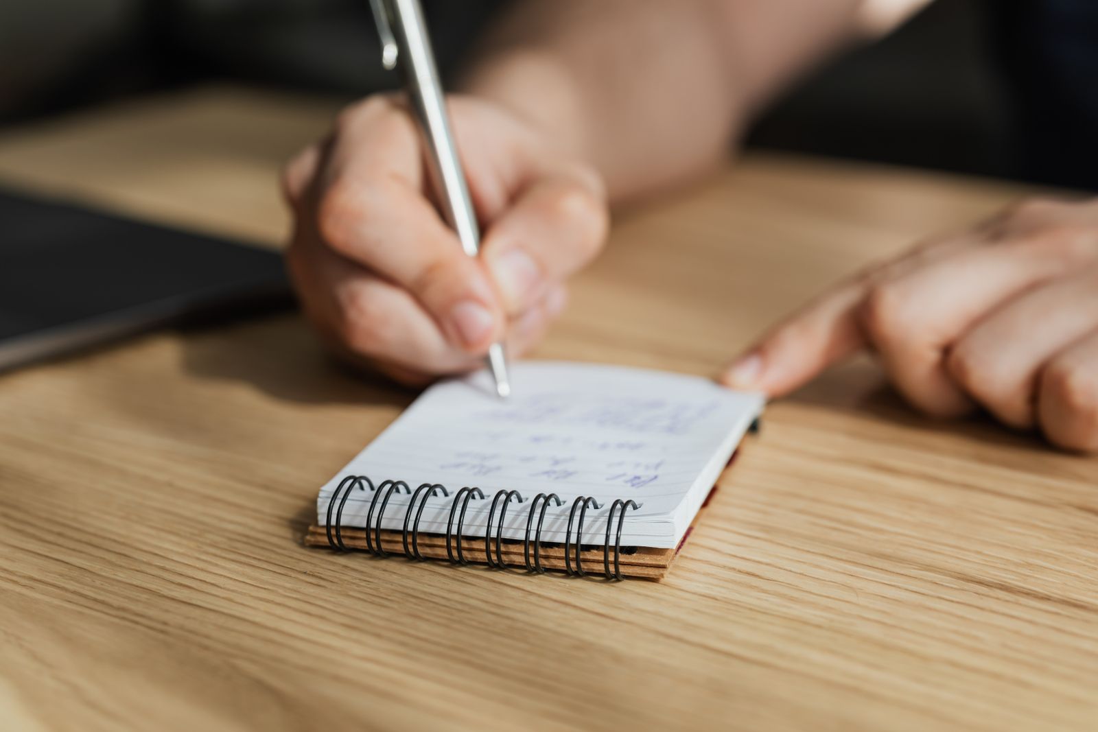 A student writing in a notebook at a wooden desk
