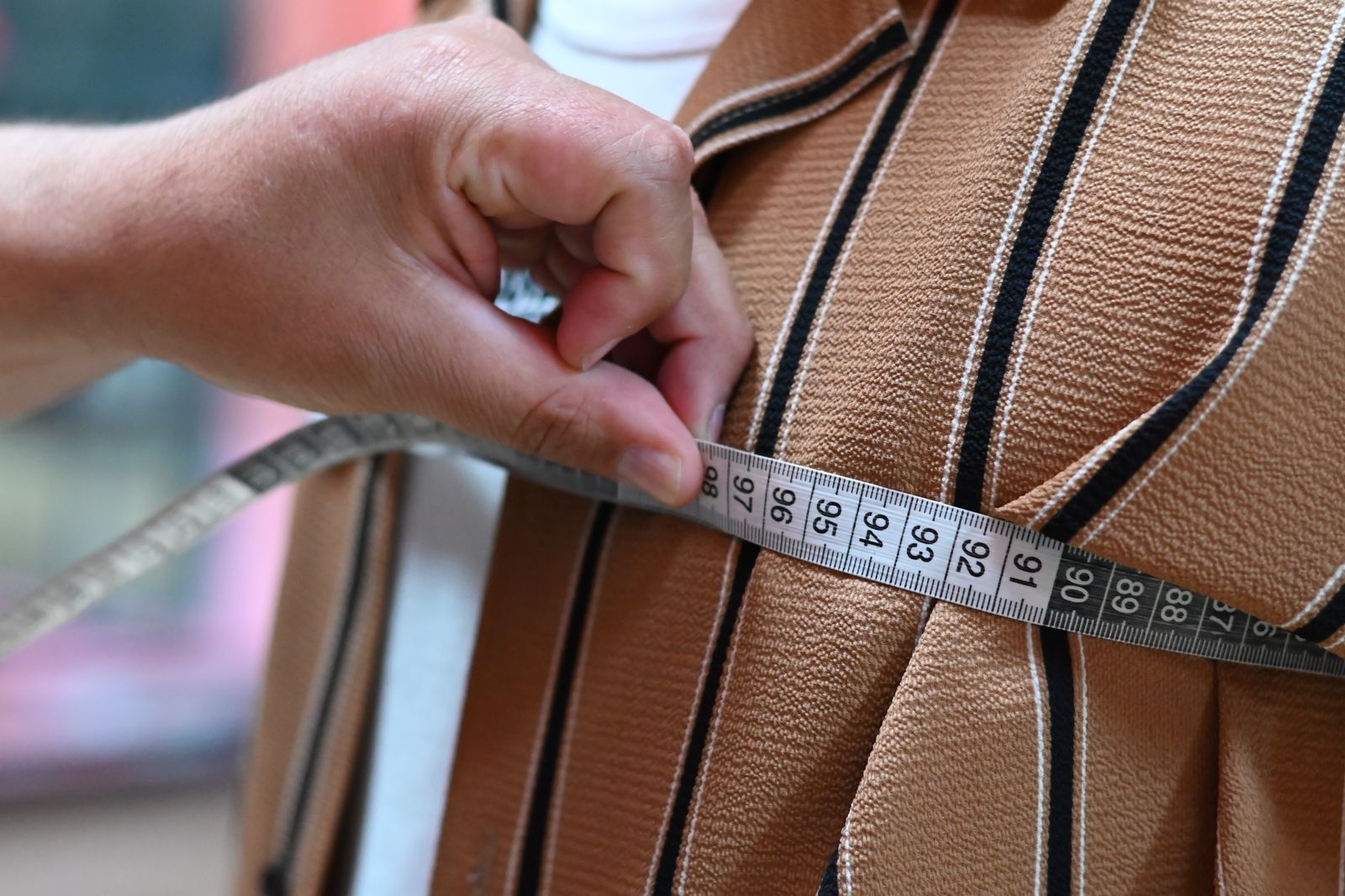 A hand holding a tape measure across striped brown cloth