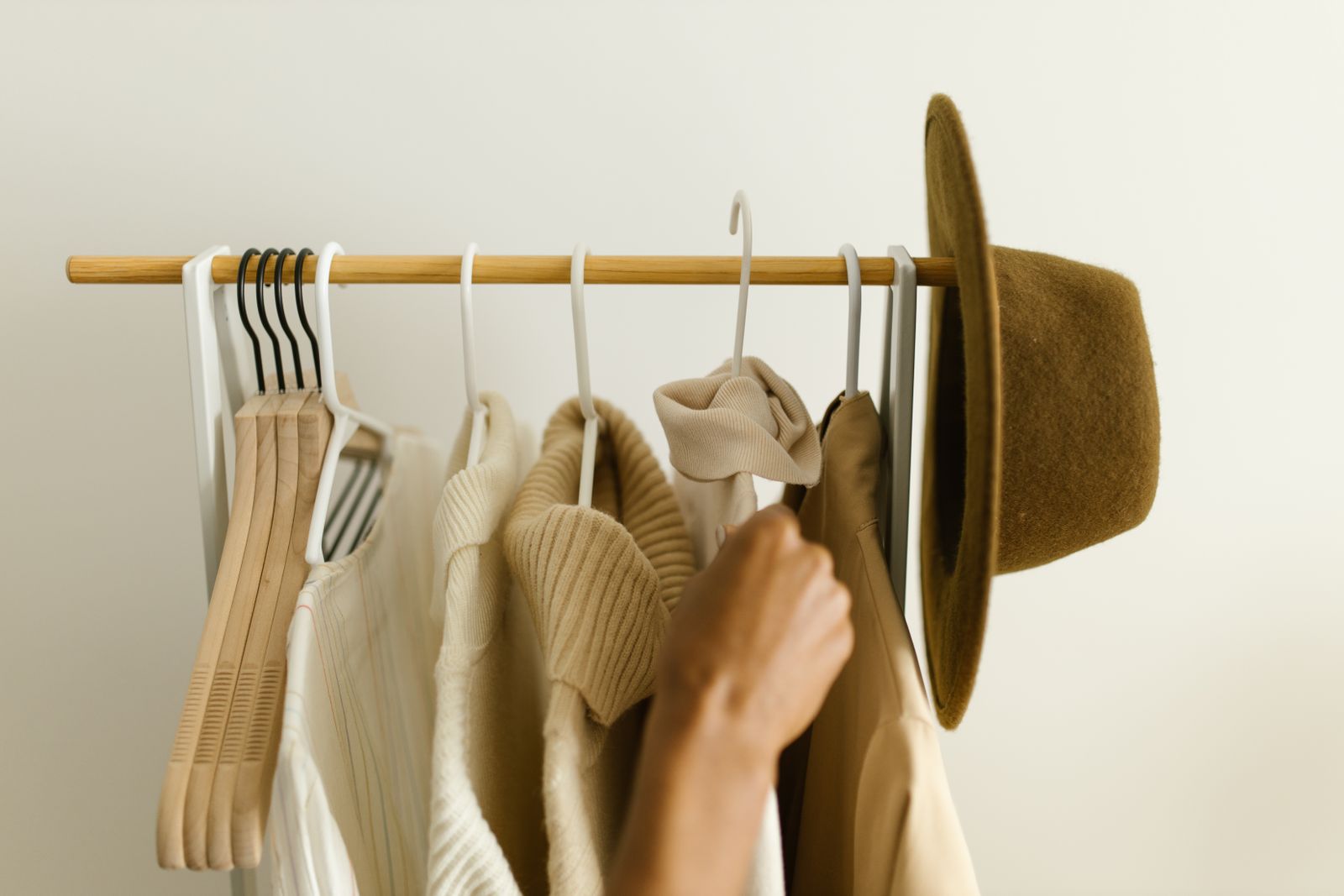 A hand choosing between cream and camel pieces on a small rail, with a felt hat on the end