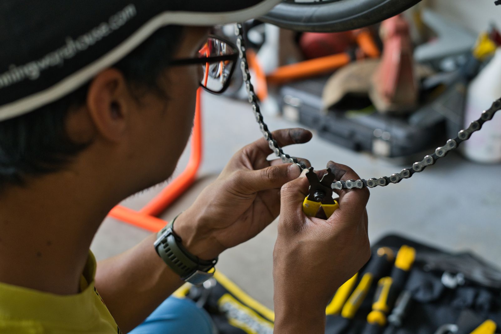 A mechanic working on a bicycle chain with tools on the bench