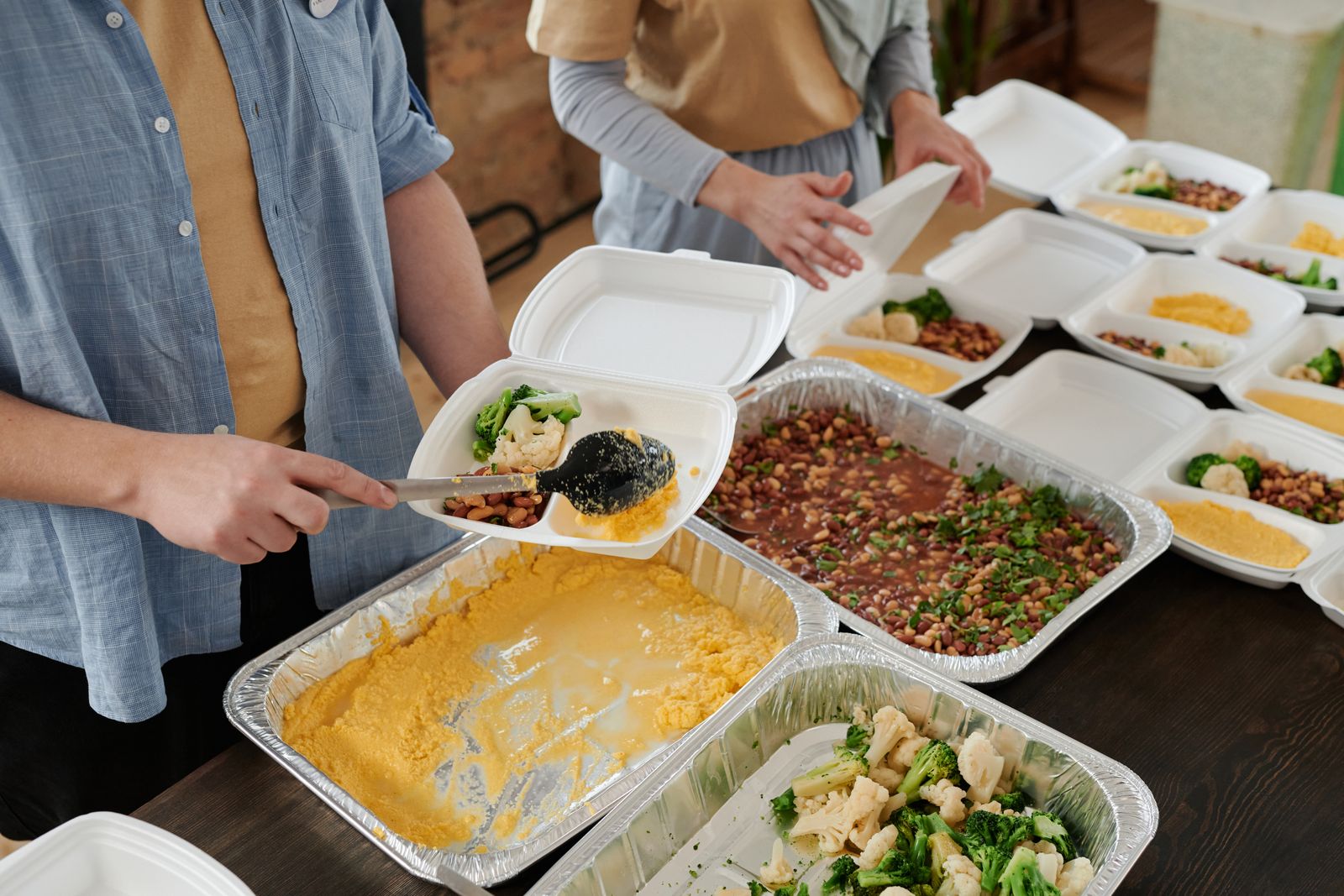 Hands filling takeaway trays with rice, vegetables and salad