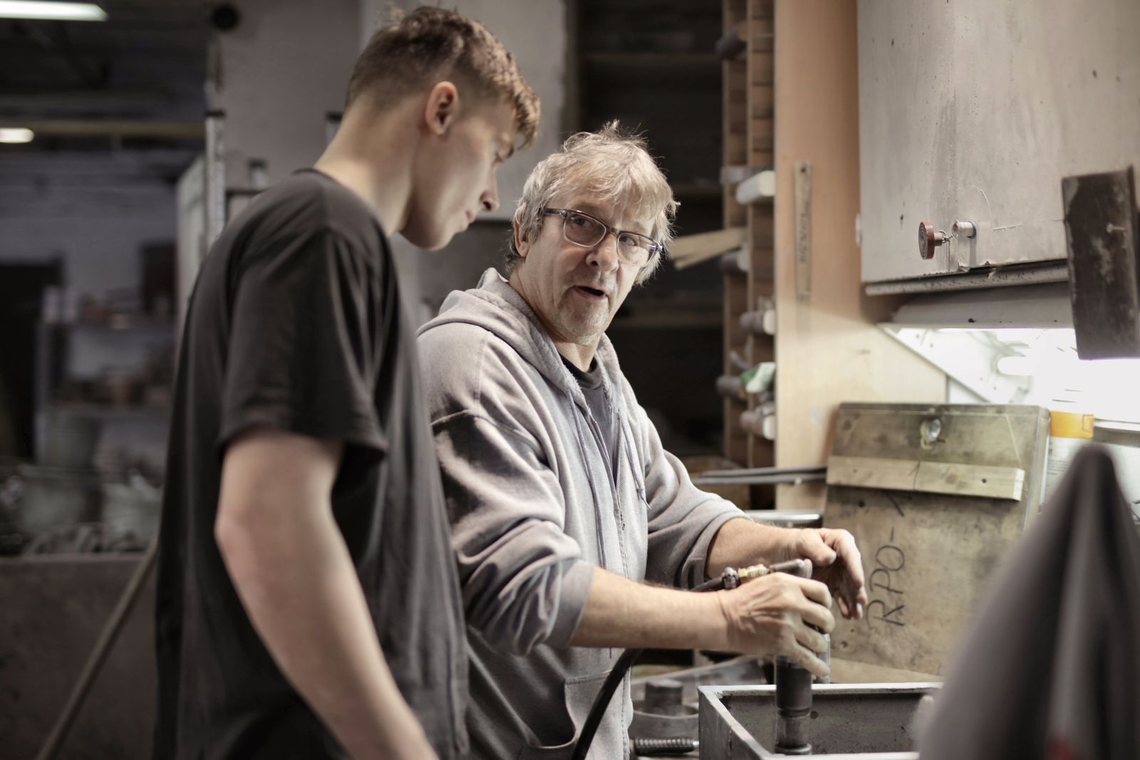 An experienced worker showing a trainee how to handle a part at a workbench
