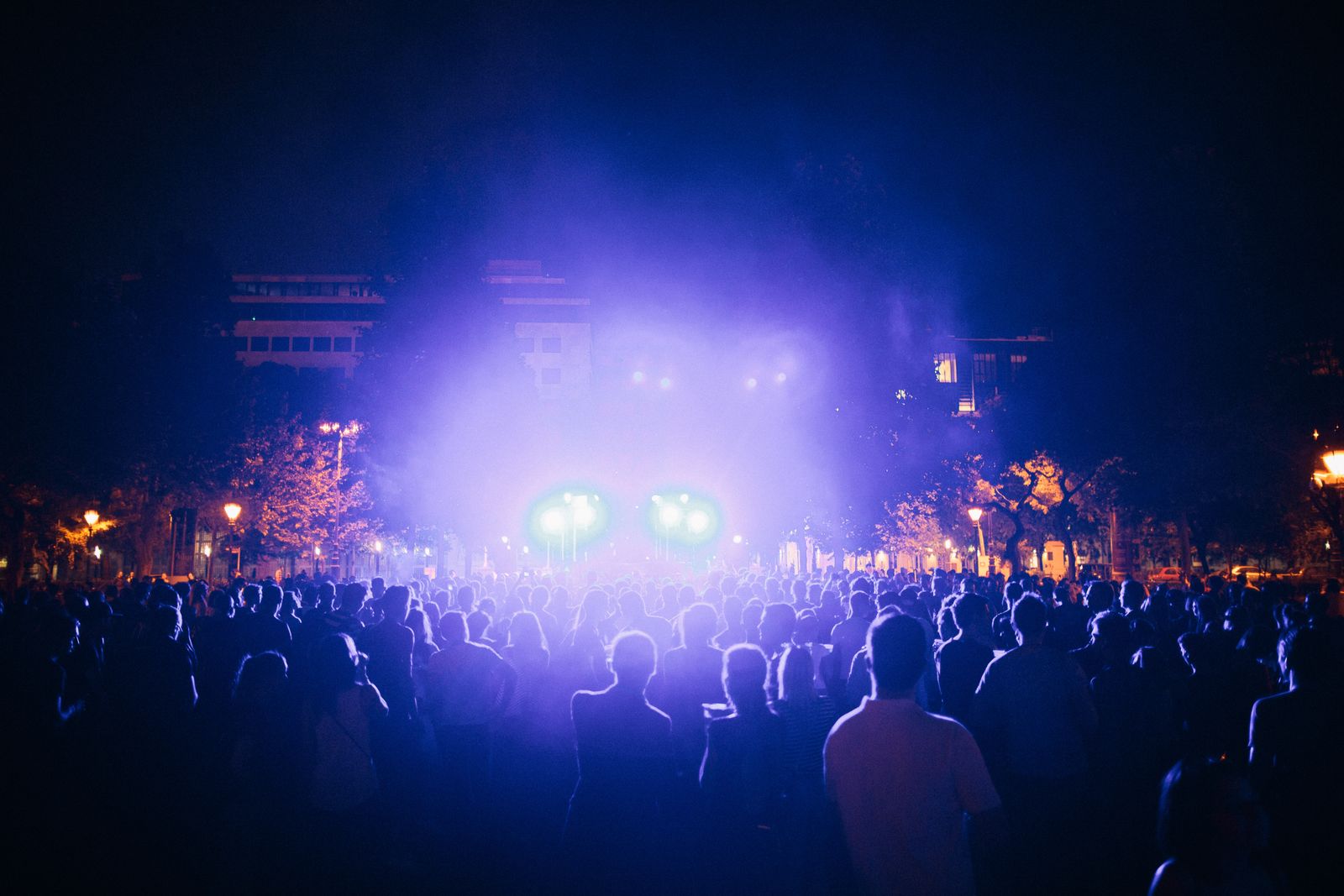 An outdoor festival crowd at night in front of a stage lit in violet