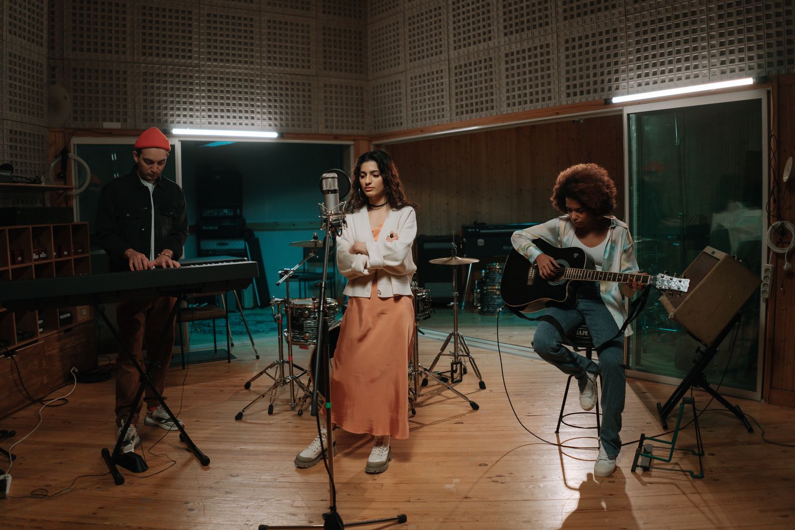 A band rehearsing in a wood-floored studio: keyboard, singer and acoustic guitar