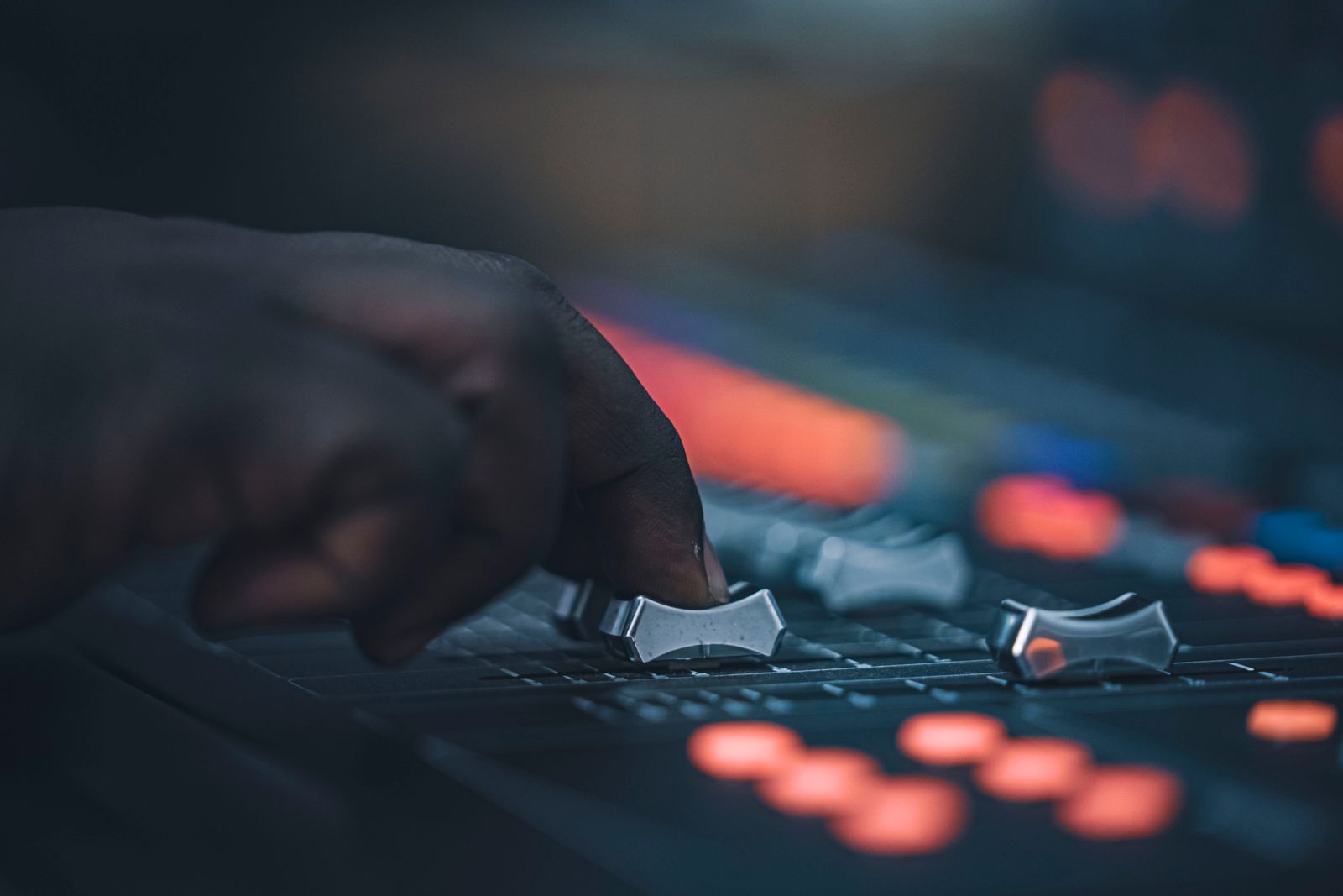 A hand moving the faders of a mixing desk in low light
