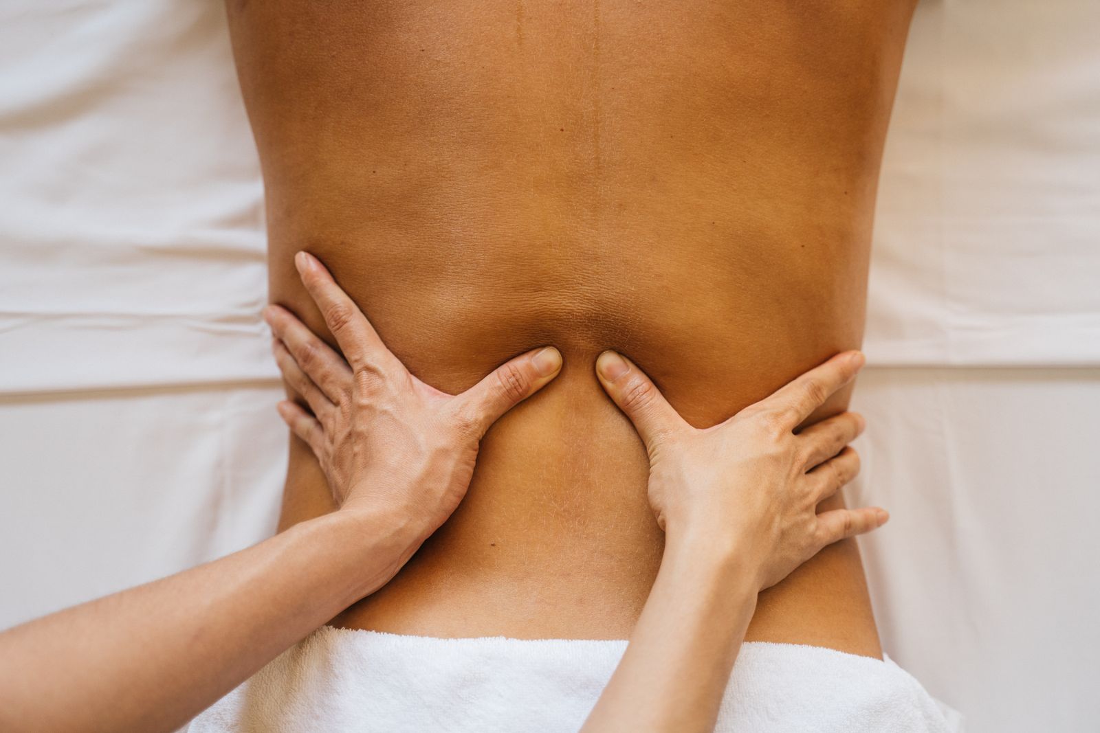 A massage therapist's hands working on a person's lower back, a white towel at the waist