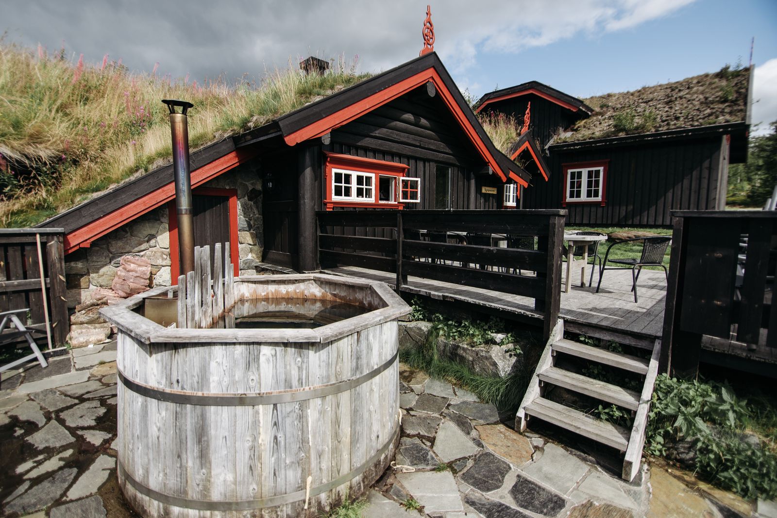 A wooden tub on a stone terrace in front of a turf-roofed timber cabin
