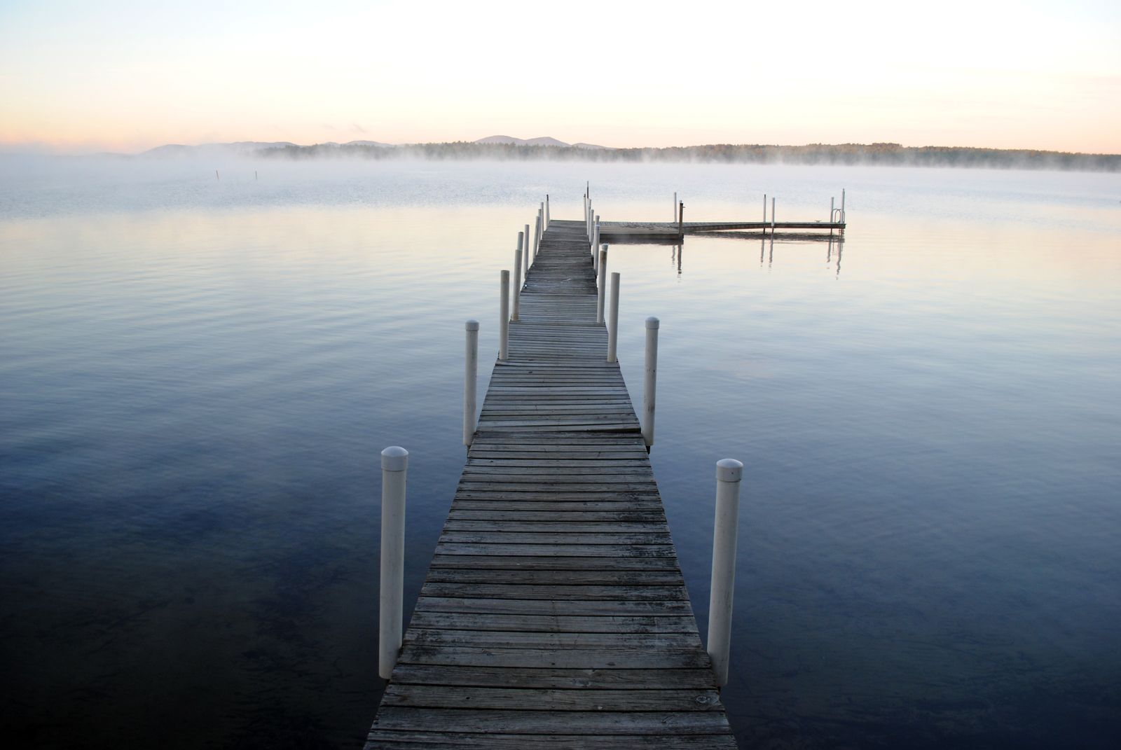 A wooden jetty running out into a still lake at dawn