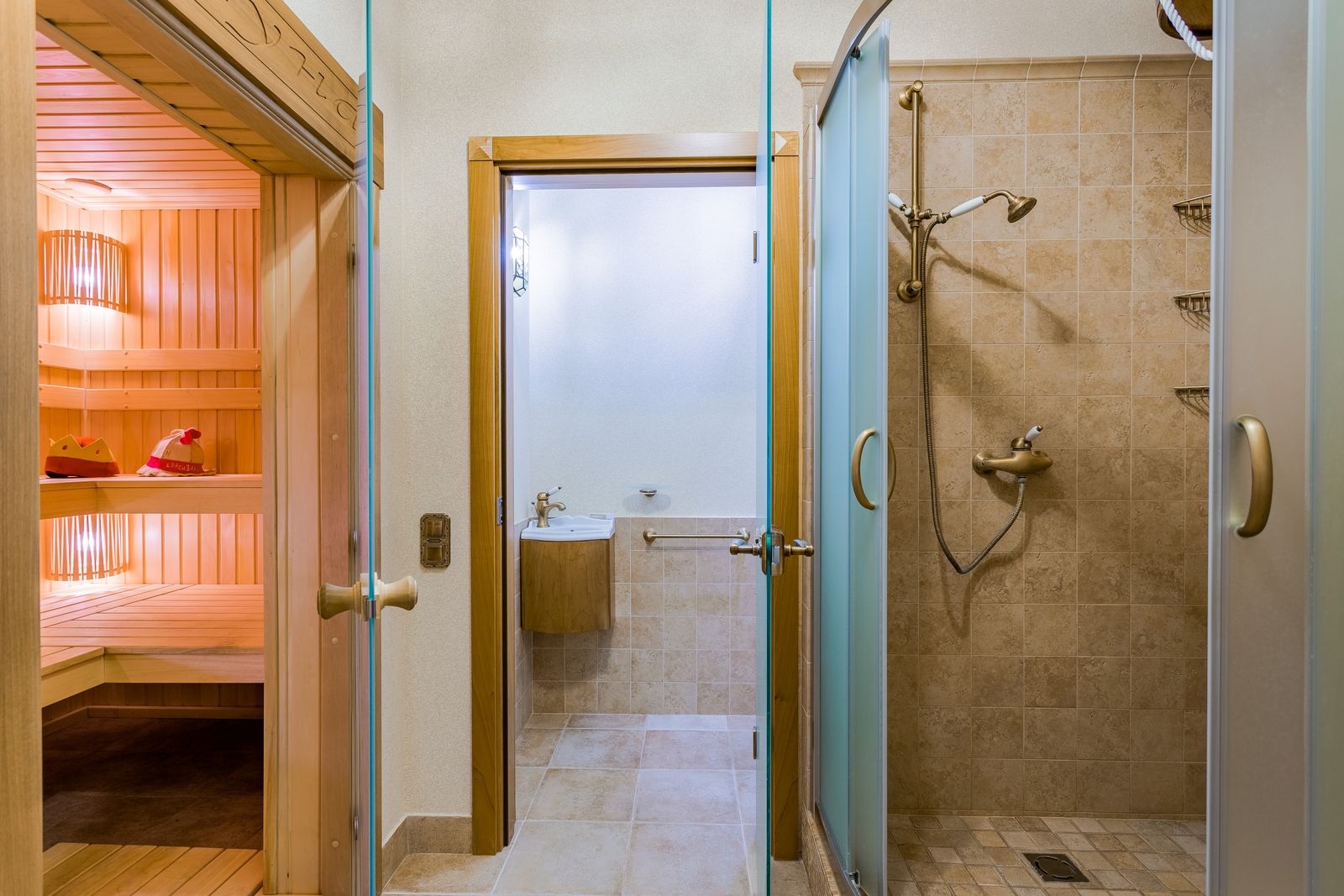 A tiled shower room beside a wooden sauna with its glass door