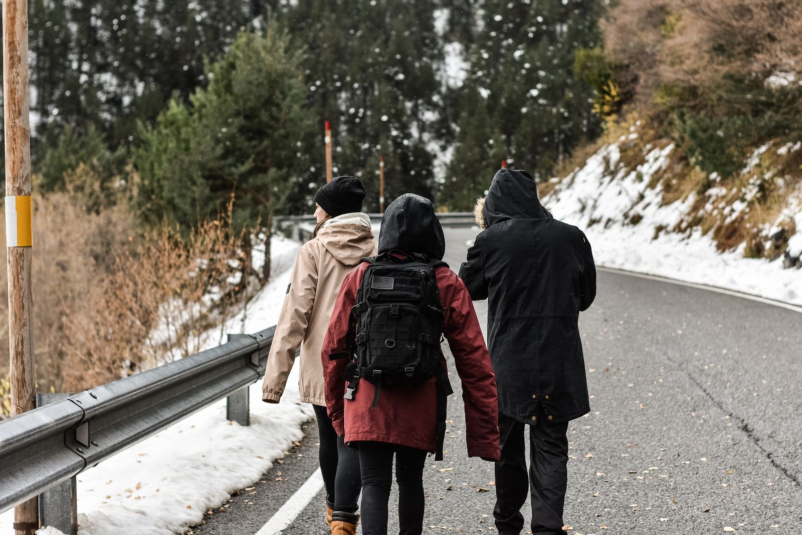 Three walkers in hooded winter jackets and a backpack on a mountain road, snow on the verges