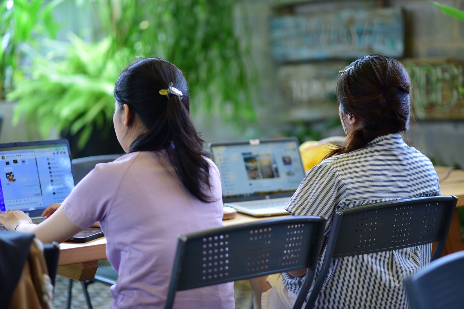 Two colleagues working on laptops at a long table in a green office