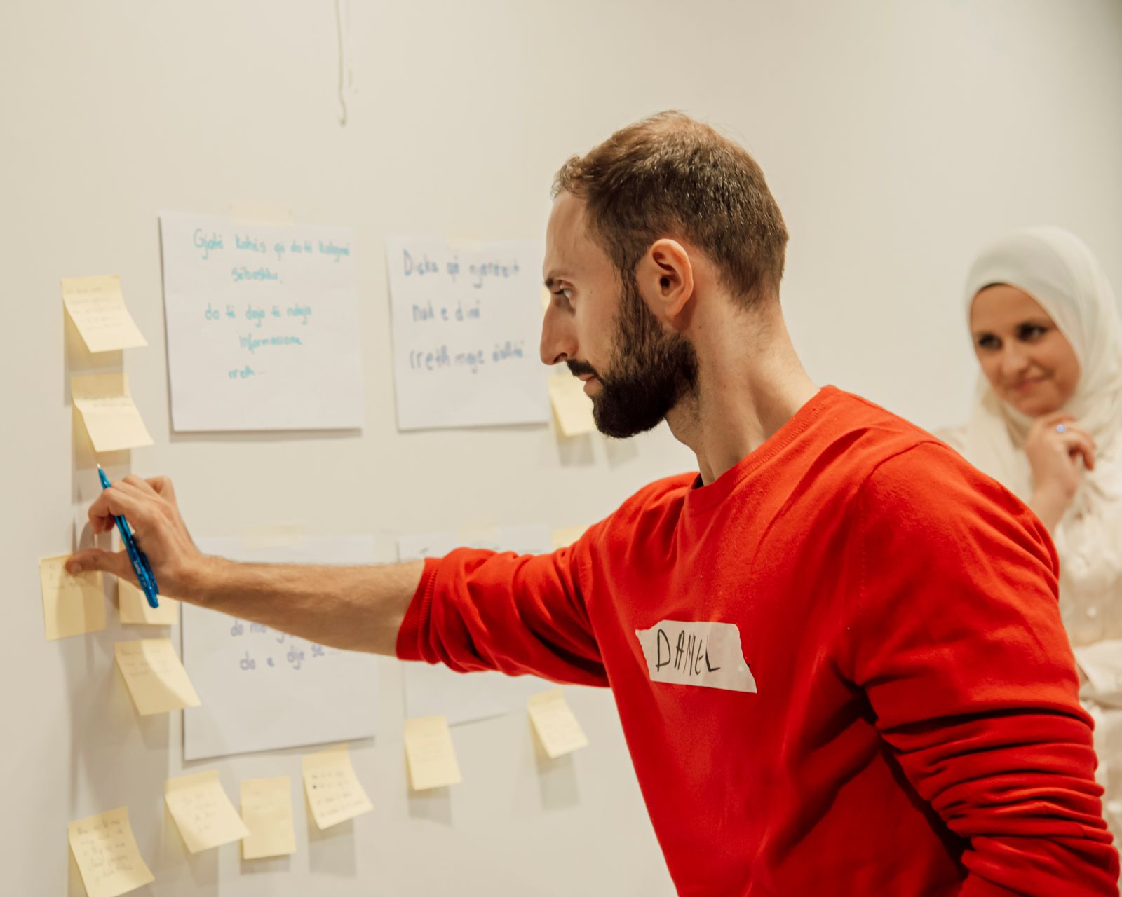 A product designer sticking notes on a wall while a colleague watches