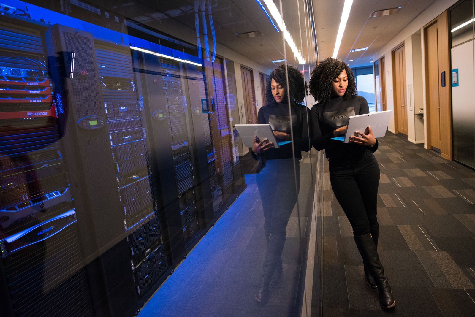 Two engineers with laptops walking along a lit row of server racks