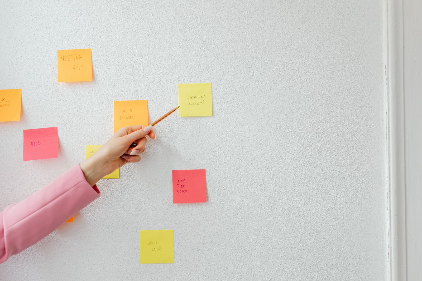 A hand arranging coloured sticky notes on a white wall
