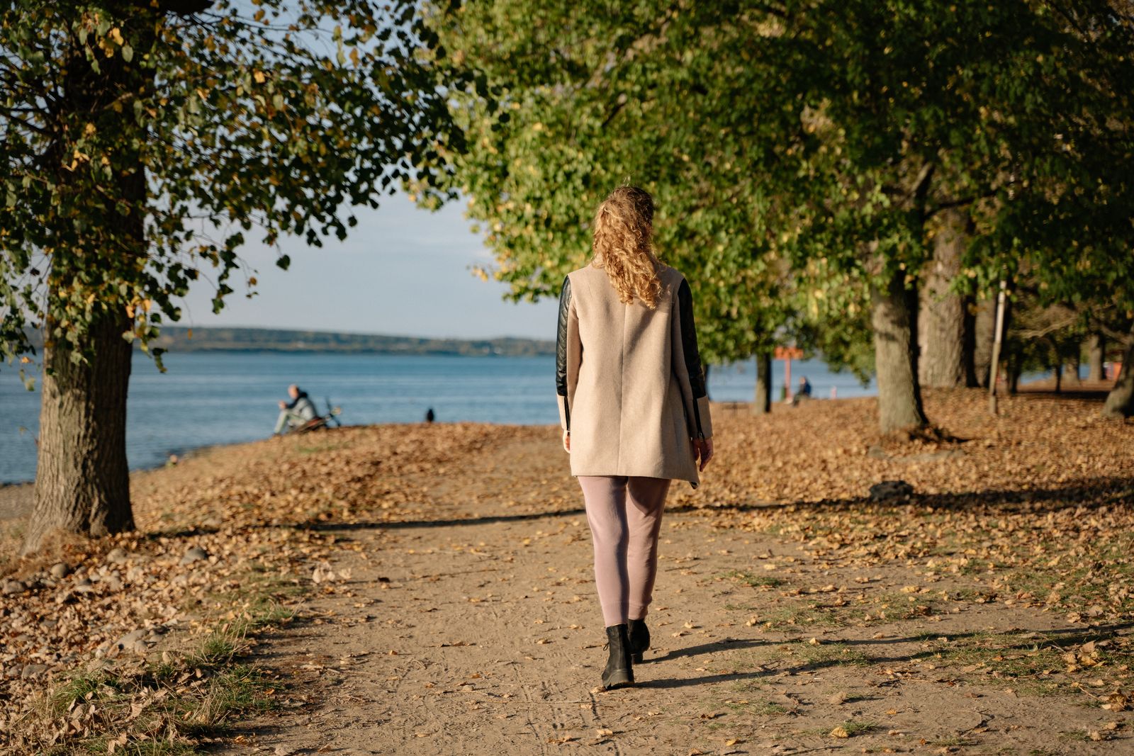 A woman walking away along a tree-lined lakeside path in autumn
