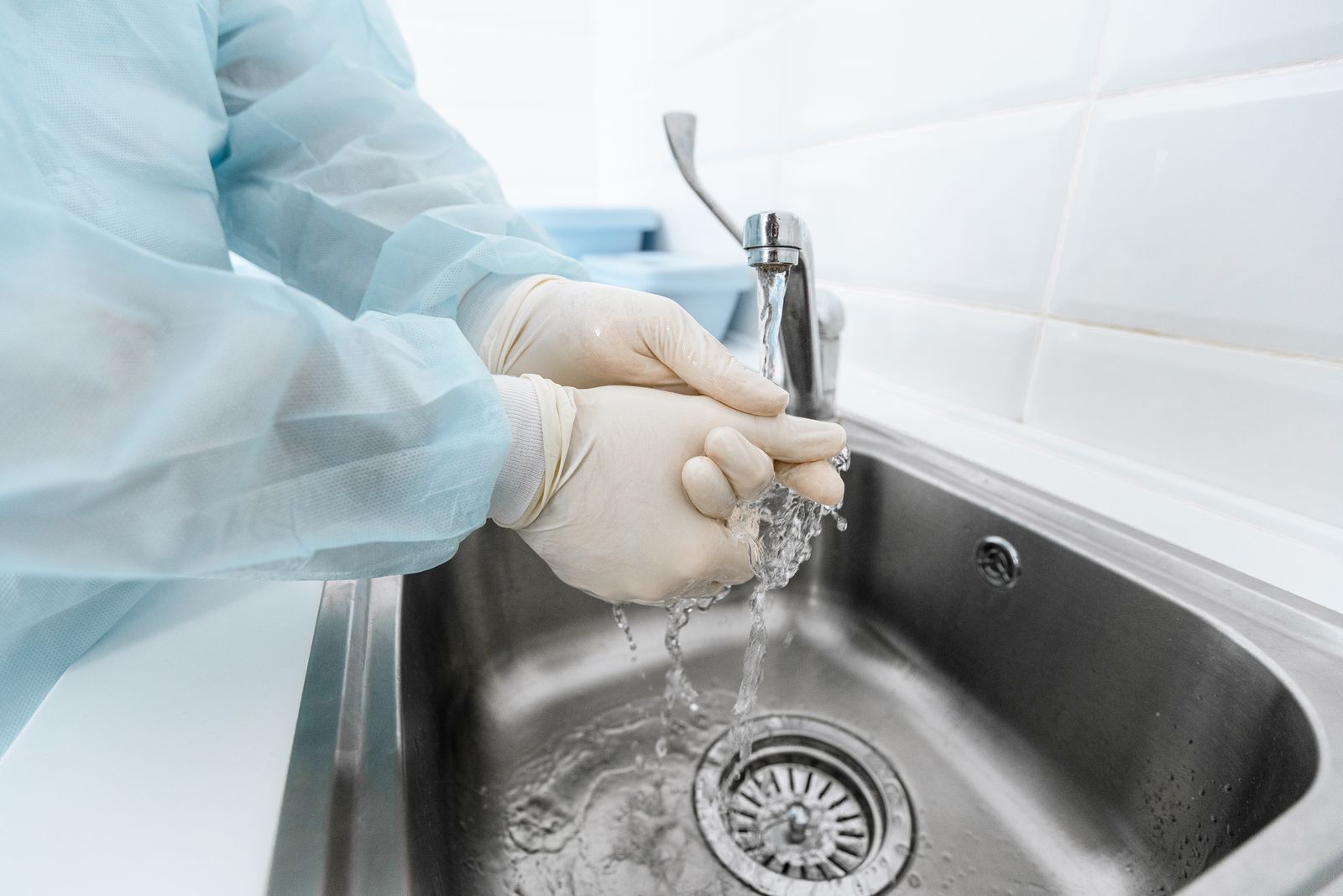 A surgeon's gloved hands under running water at a steel scrub sink