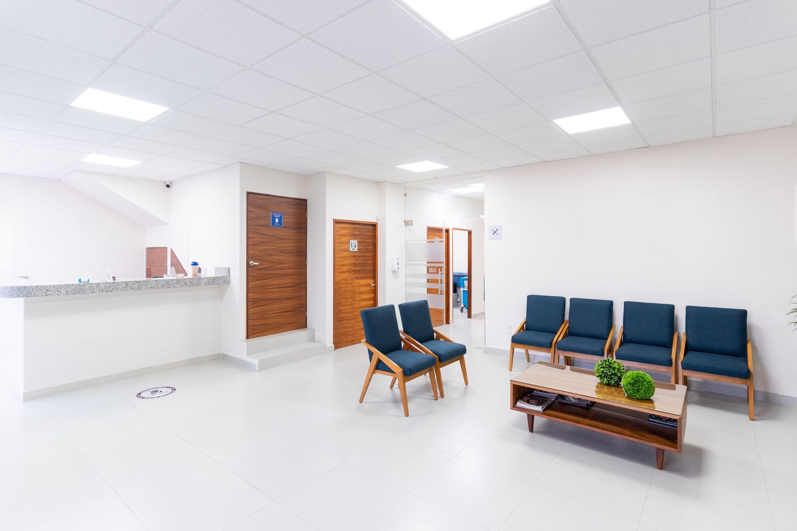 A quiet clinic waiting room with blue chairs, a low table and white walls
