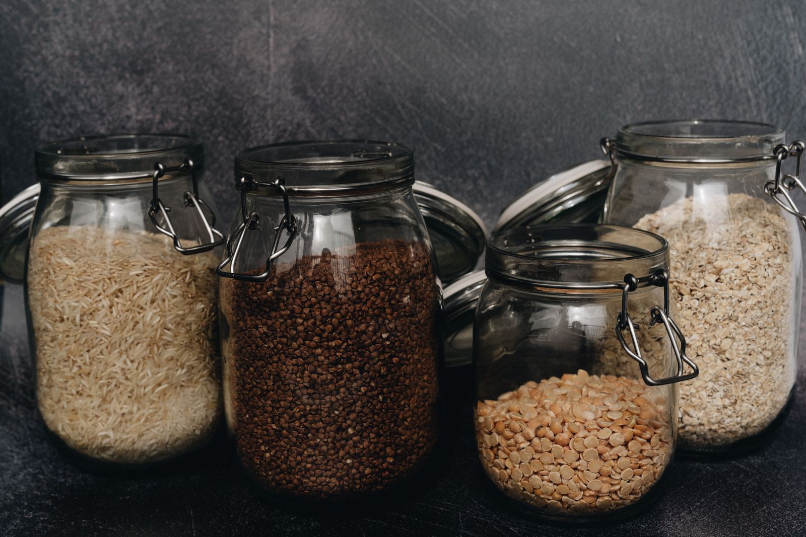 Glass jars of buckwheat, lentils, rice and oats on a dark table