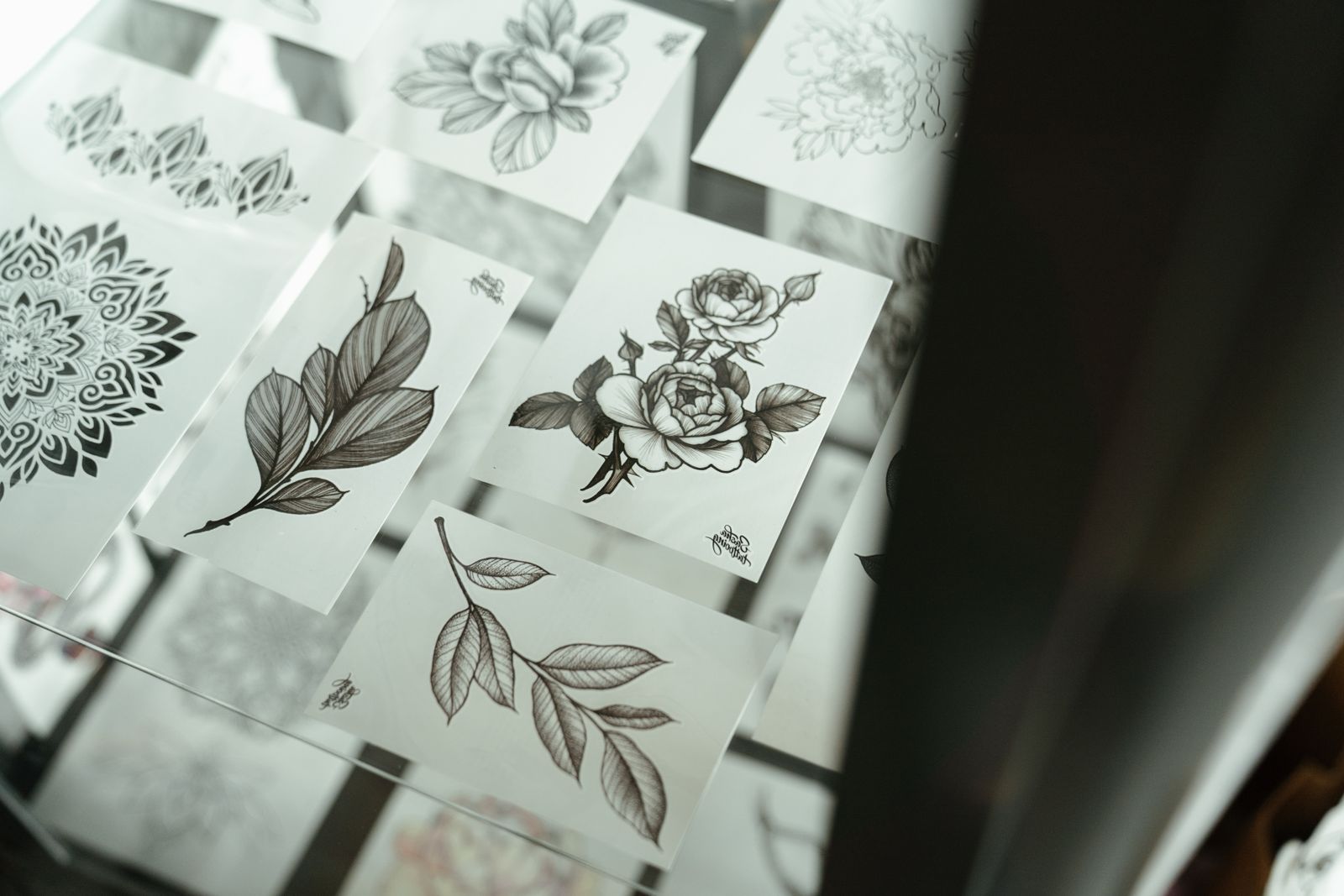 Sheets of floral and abstract tattoo designs laid out on a table in the studio