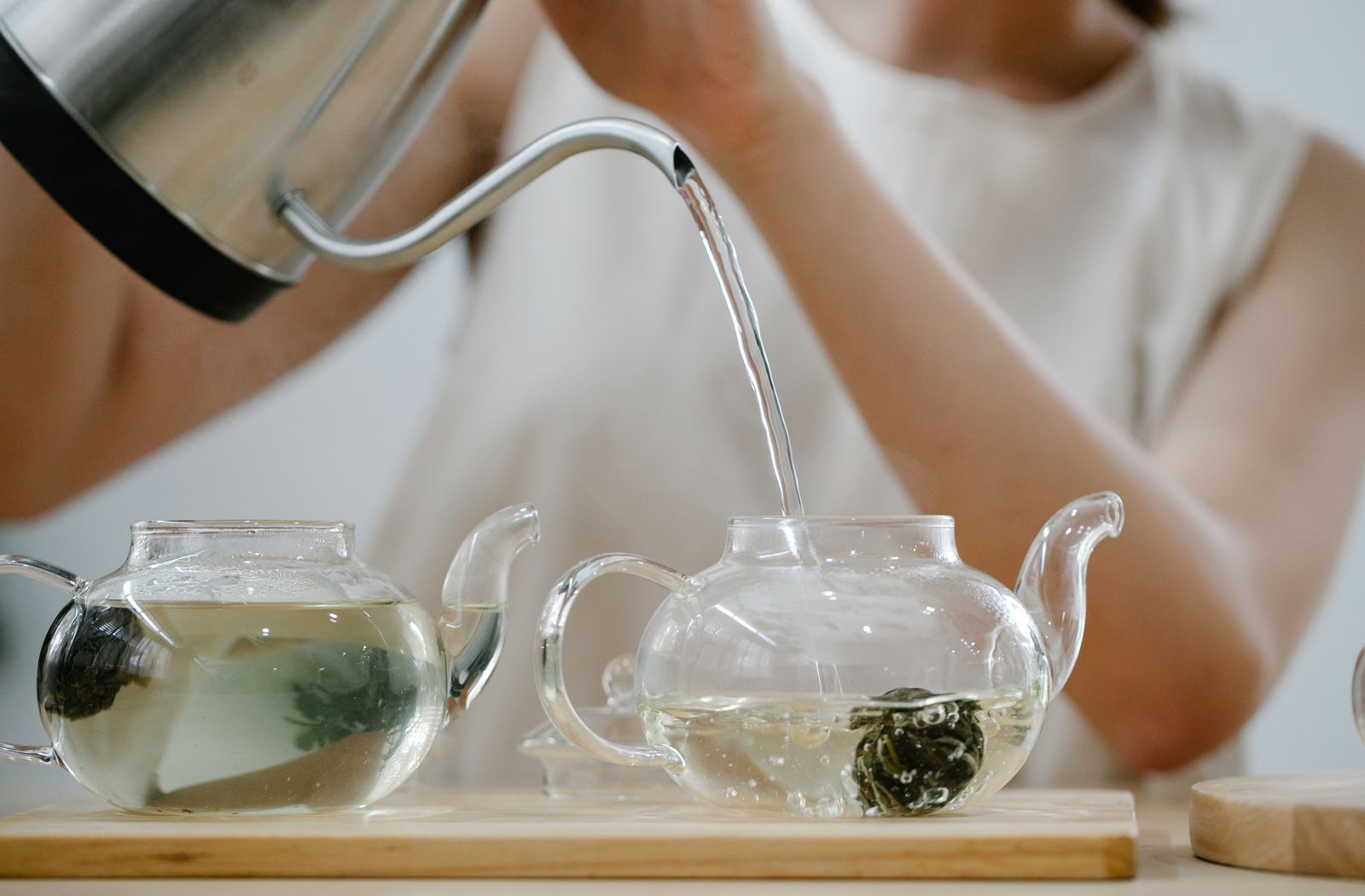 Hot water poured from a kettle into glass teapots of green tea
