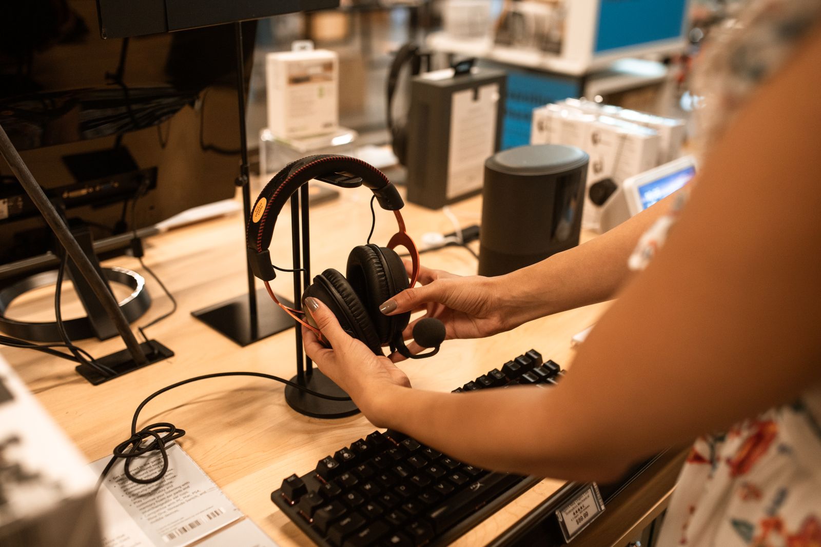 A customer's hands lifting headphones from a stand on a demo table in an electronics shop