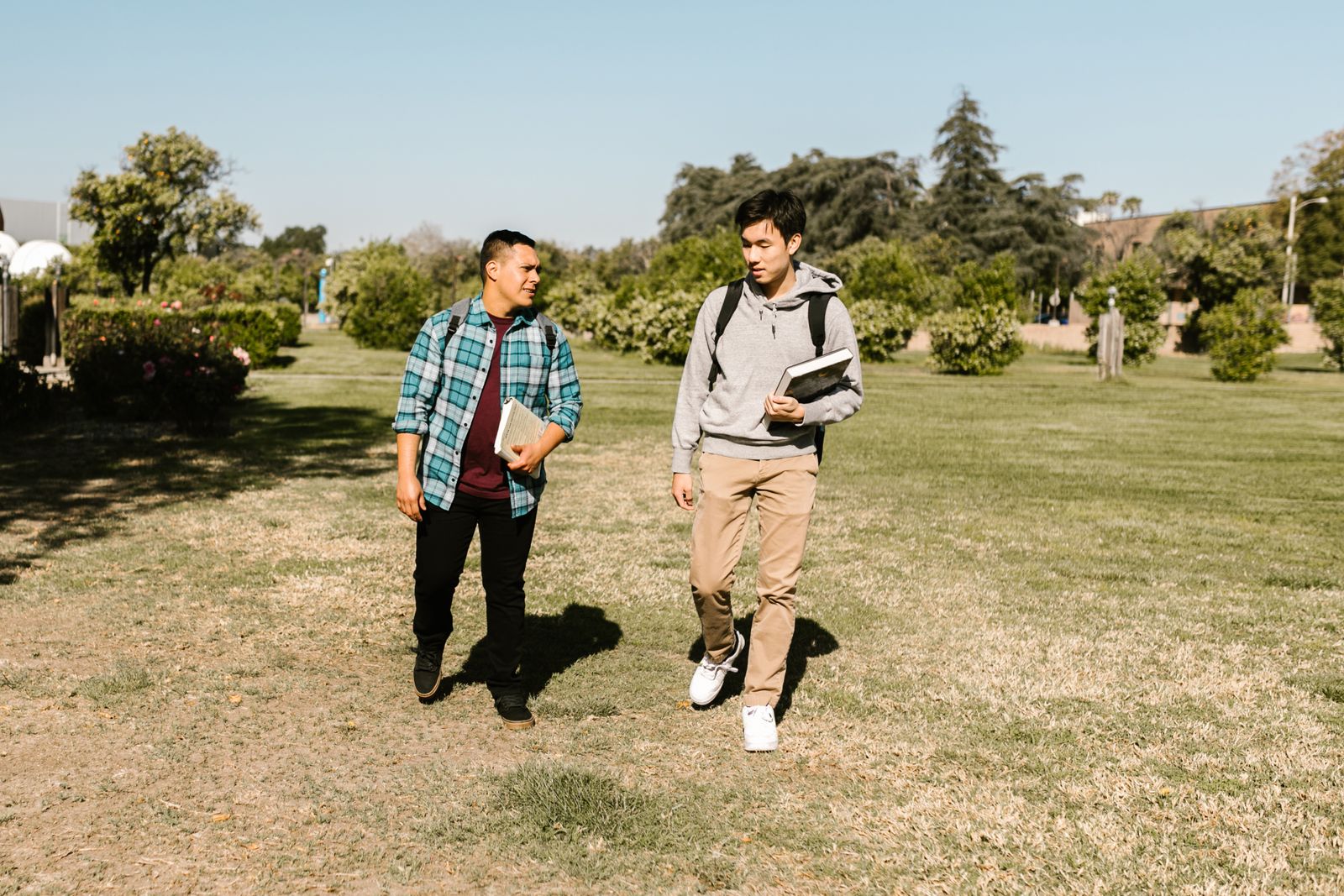 Two students walking across a sunny campus lawn with books